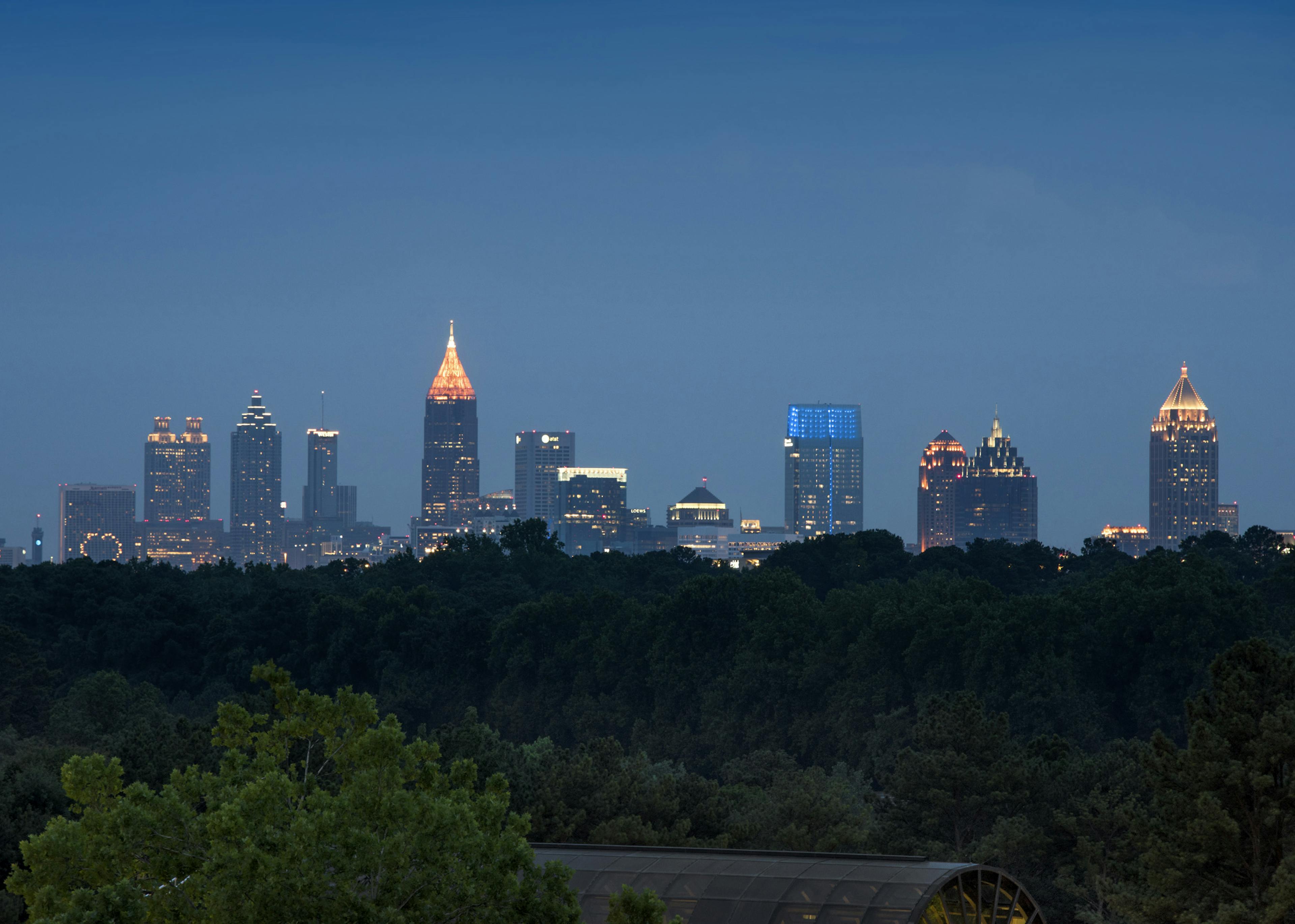 Evening view of the Buckhead Atlanta skyline with lit office buildings in the distance and lush trees in foreground