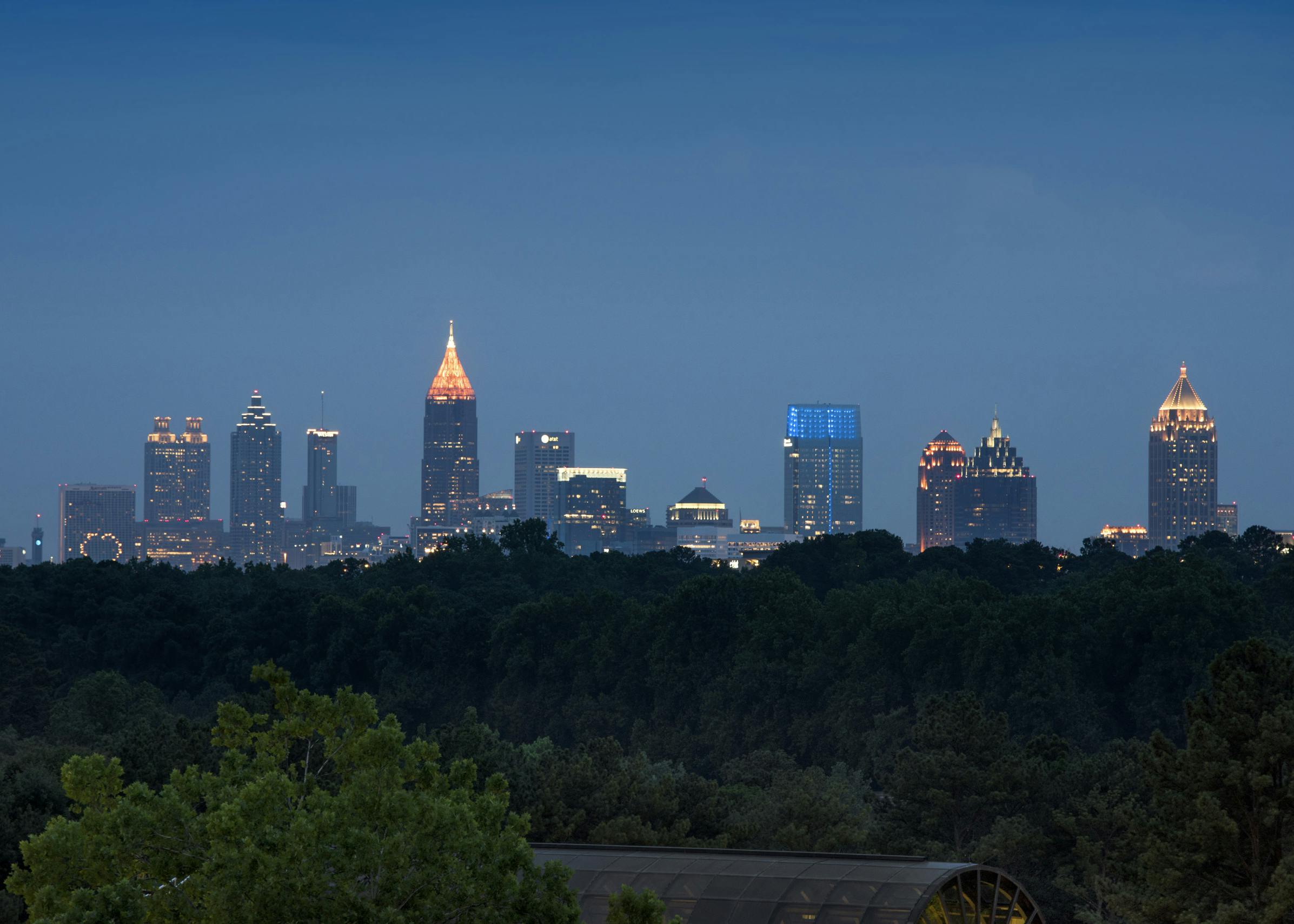 Evening view of the Buckhead Atlanta skyline with lit office buildings in the distance and lush trees in foreground