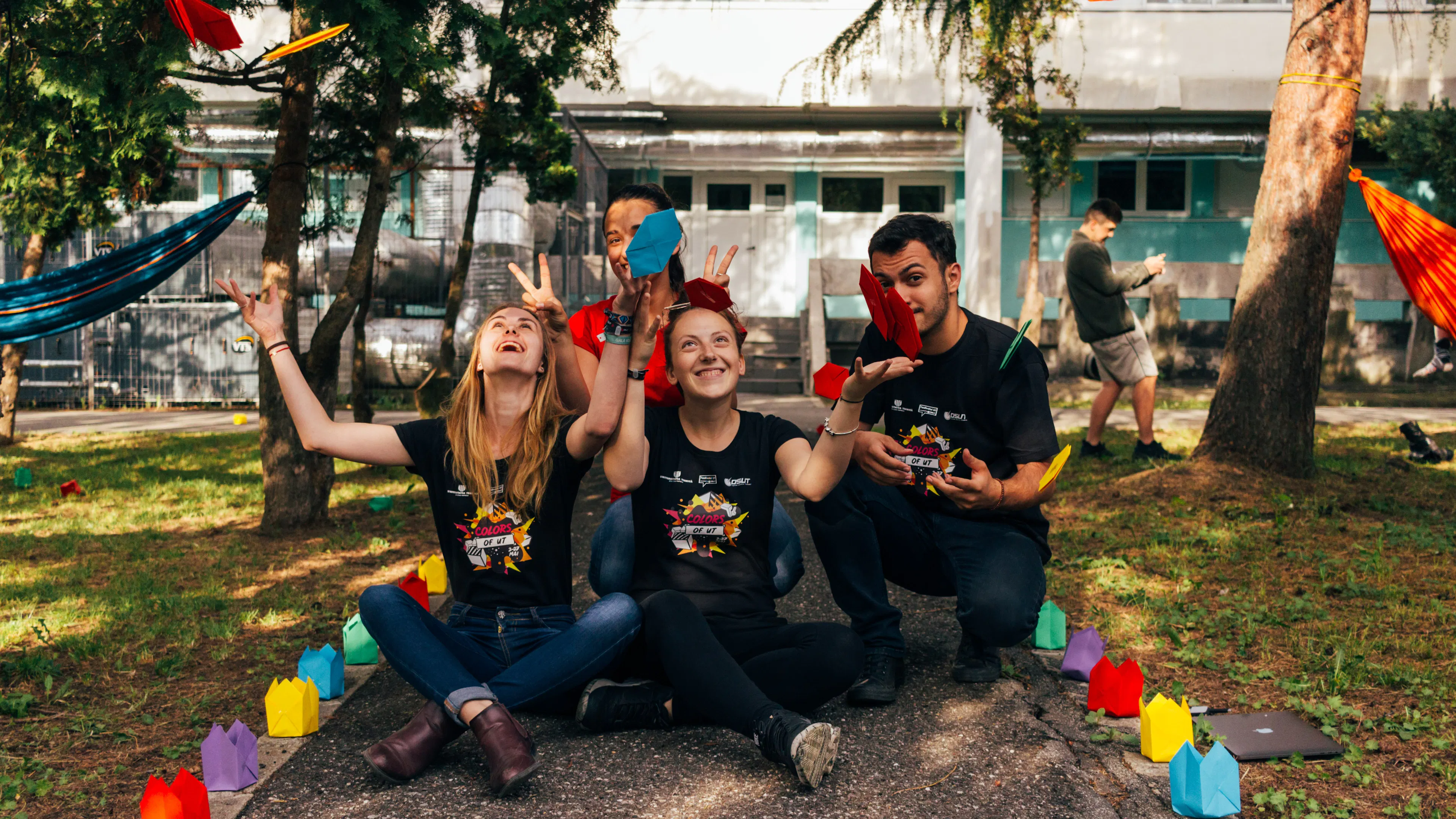 Four people sitting on a sidewalk throwing confetti into the air