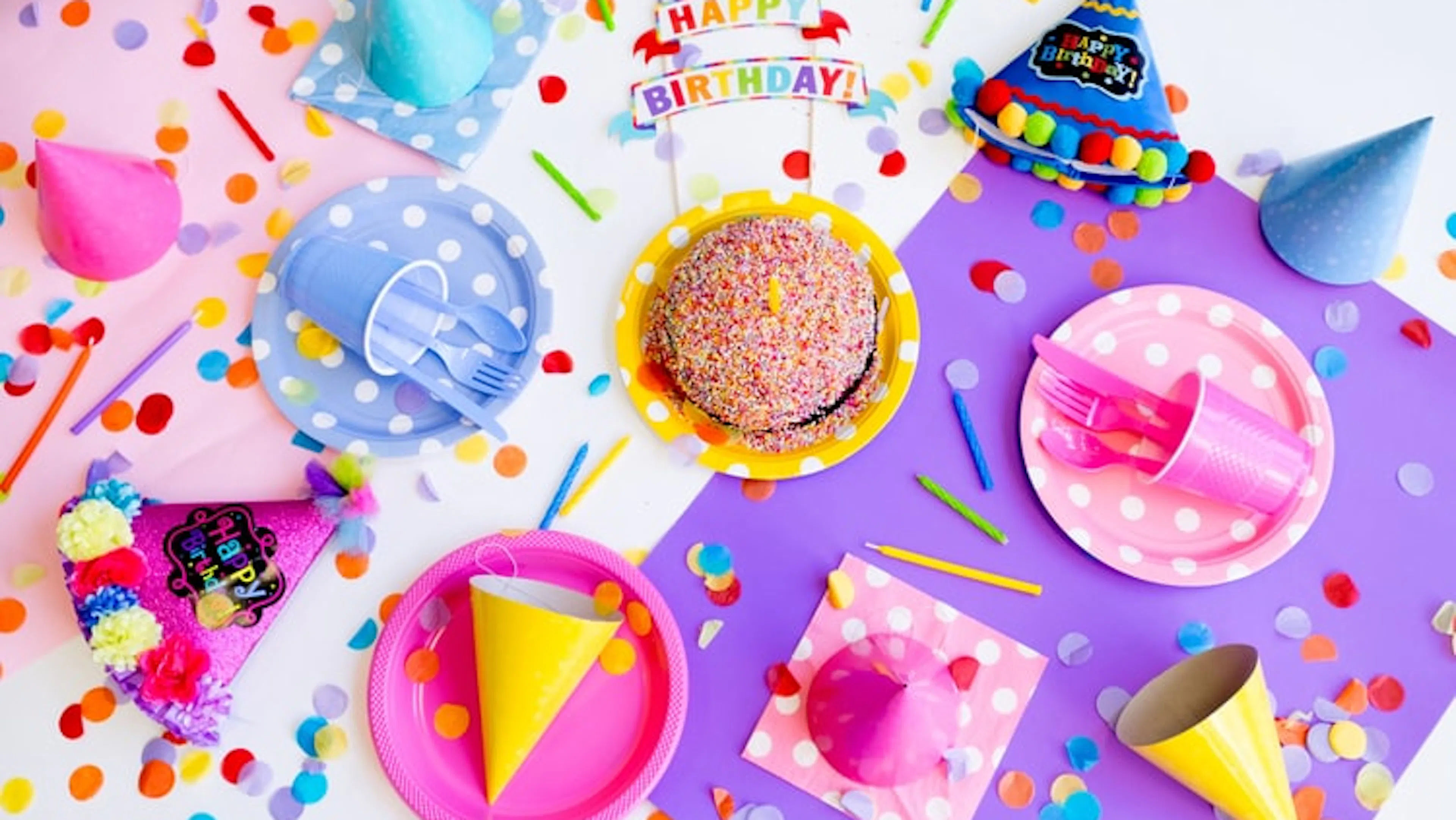 Pink and yellow party plates with cupcakes and party hats around them