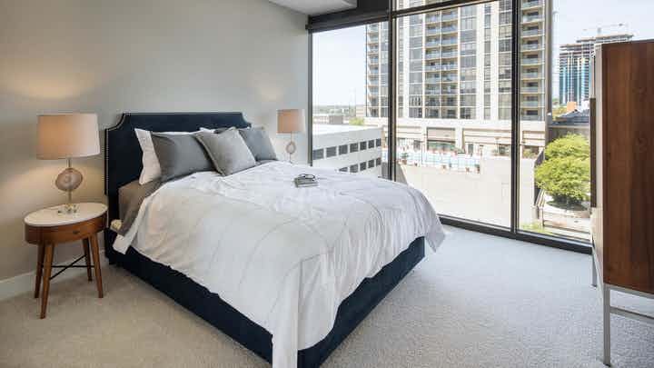 Interior of bedroom at AMLI Arts Center with grey and white bedding and floor to ceiling windows with a daytime city view