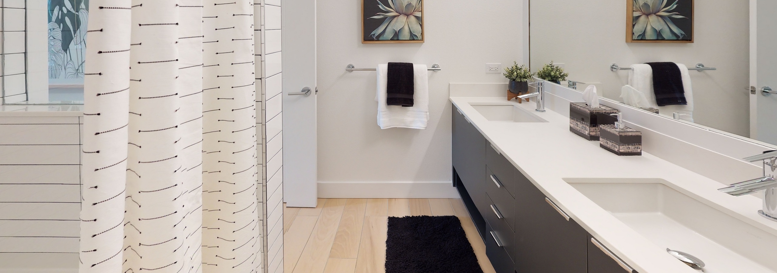 Interior view of AMLI Park West apartment bathroom with double dark wood vanity with large mirror above and wood plank floors
