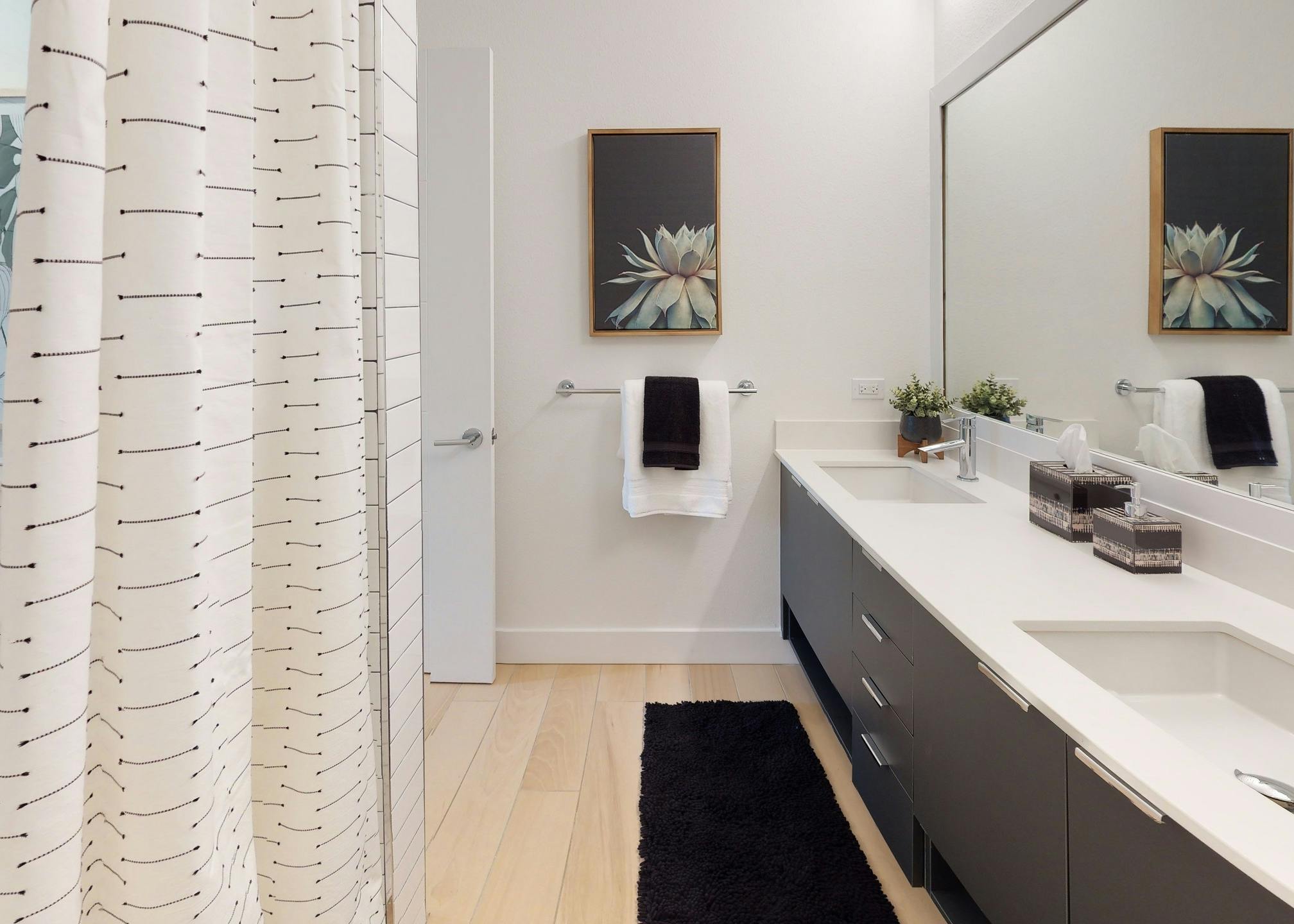 Interior view of AMLI Park West apartment bathroom with double dark wood vanity with large mirror above and wood plank floors
