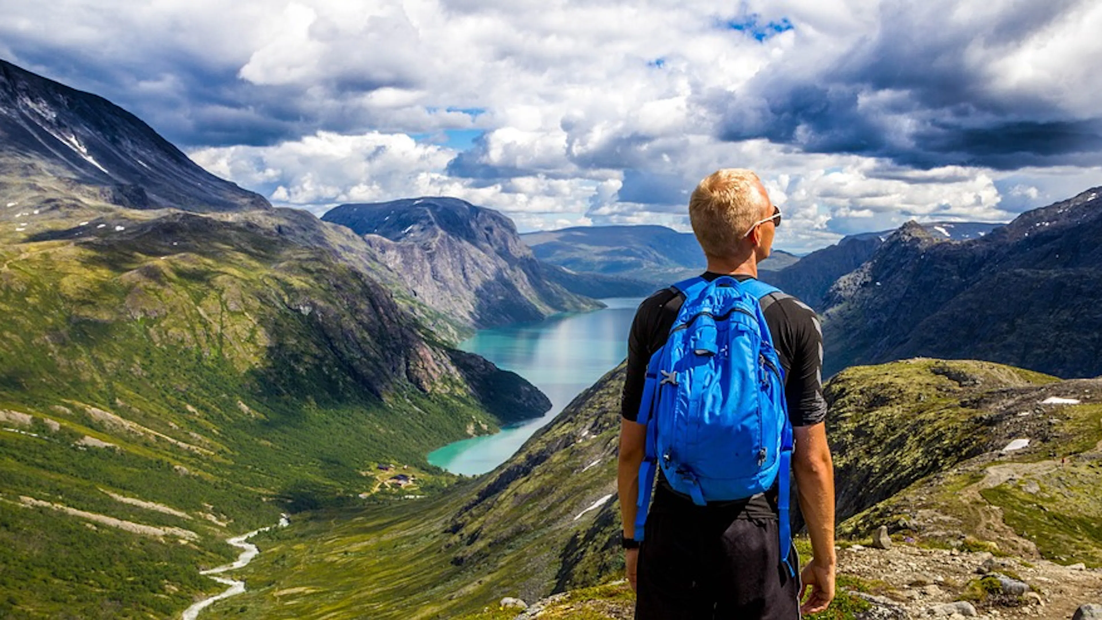 A hiker looking out over an expansive valley with a crystal blue lake in the center of a group of mountains