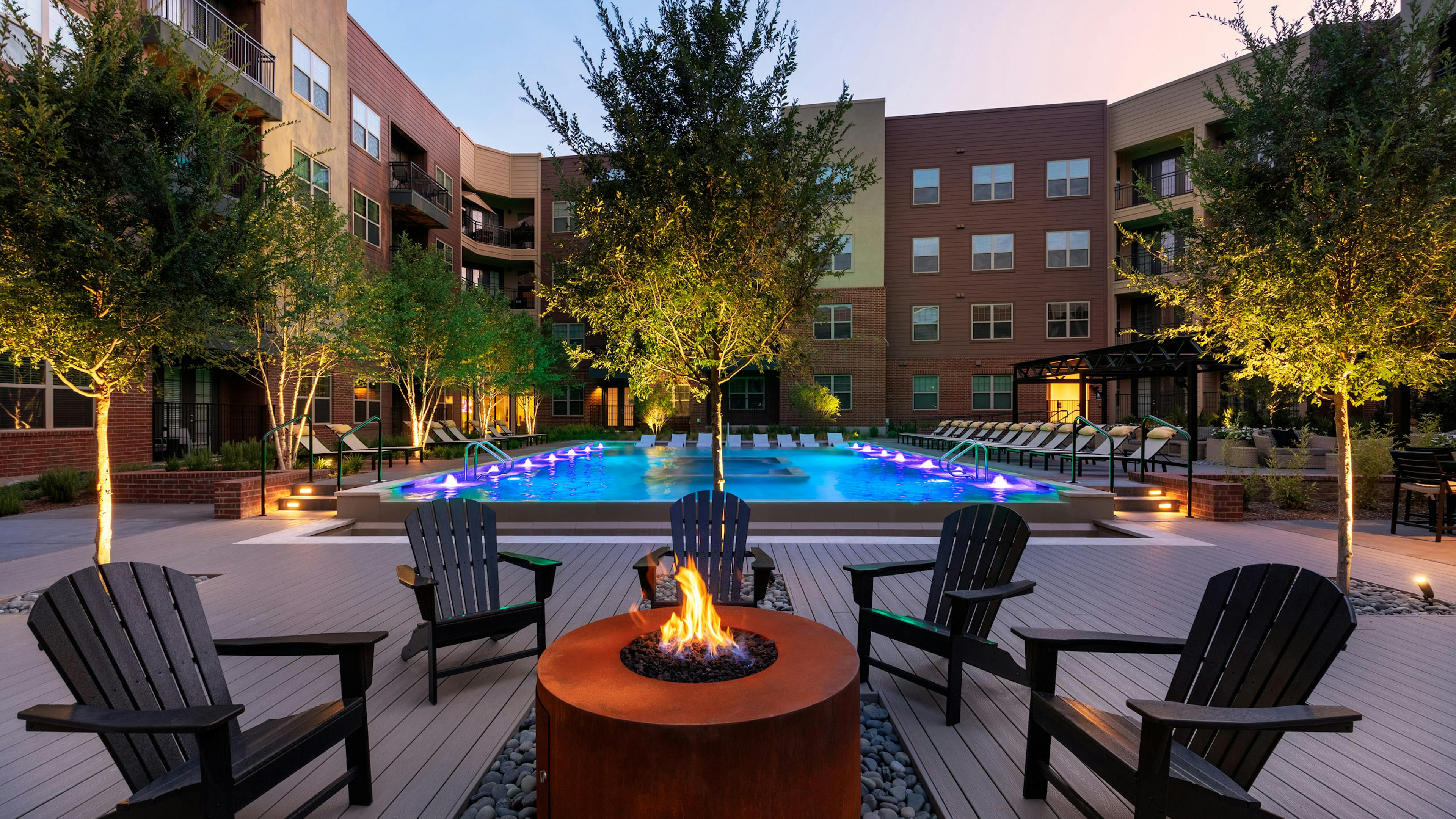 Evening view of AMLI Grapevine dark orange poolside fire pit with black surrounding seating and the pool in the background