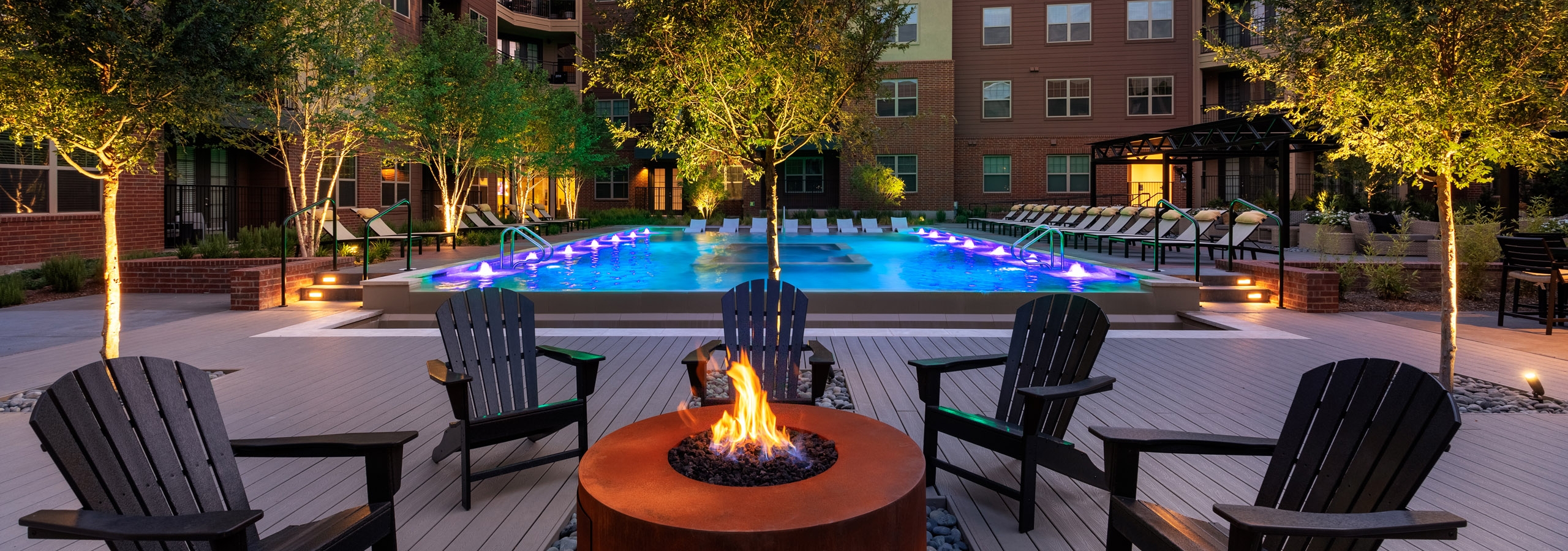 Evening view of AMLI Grapevine dark orange poolside fire pit with black surrounding seating and the pool in the background