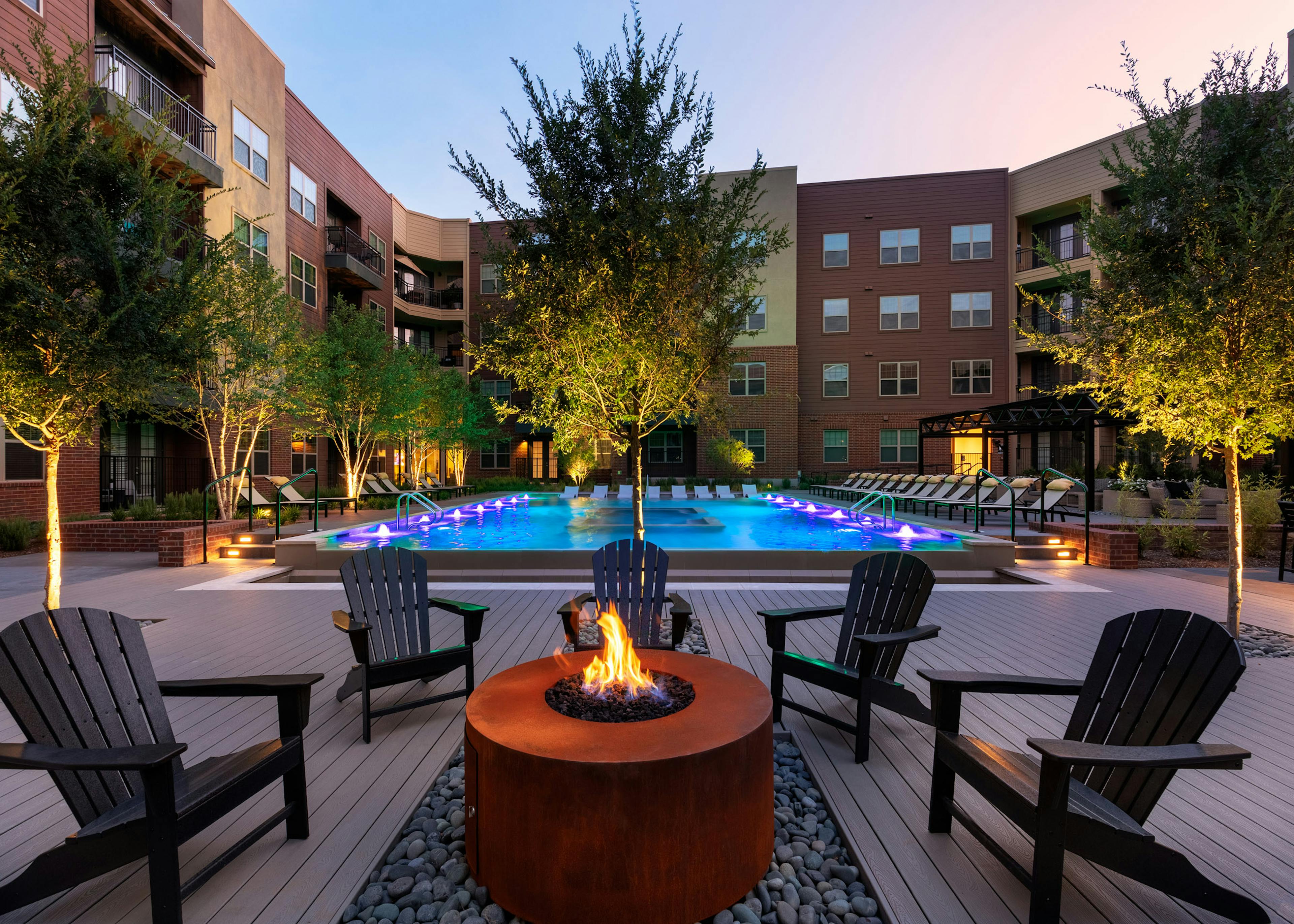 Evening view of AMLI Grapevine dark orange poolside fire pit with black surrounding seating and the pool in the background