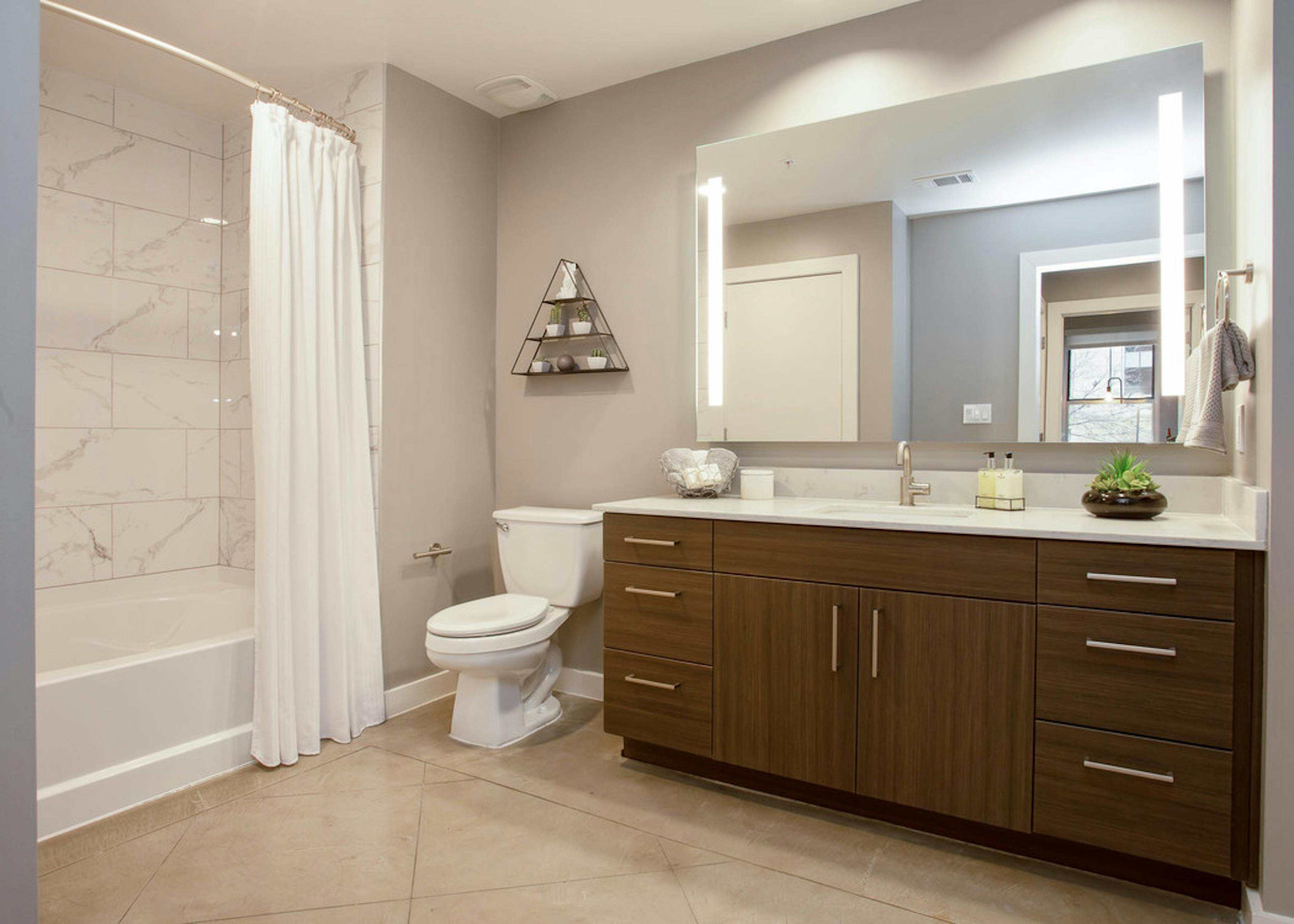 Interior of AMLI Downtown bathroom with shower tub with marble wall tile and a toilet next to a long dark wood vanity sink
