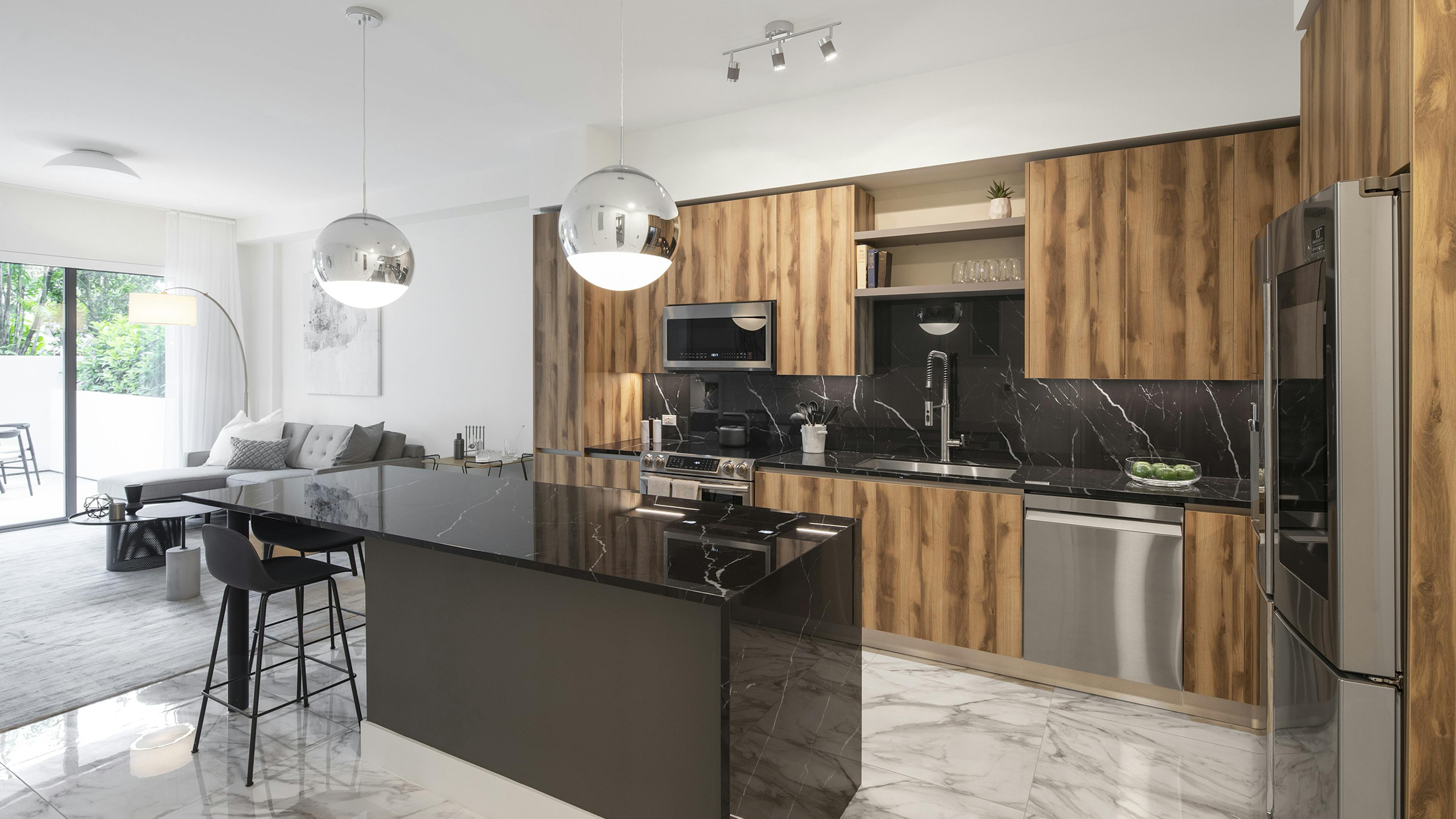 Interior view of AMLI Midtown Miami apartment kitchen with dark marble island and zebra wood cabinets and living room at left