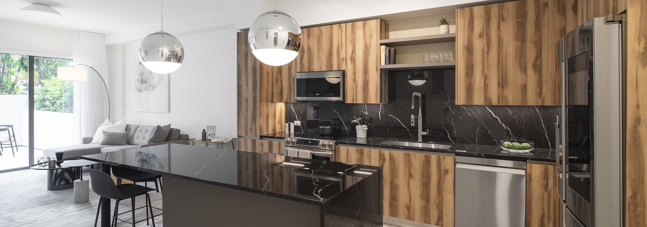 Interior view of AMLI Midtown Miami apartment kitchen with dark marble island and zebra wood cabinets and living room at left
