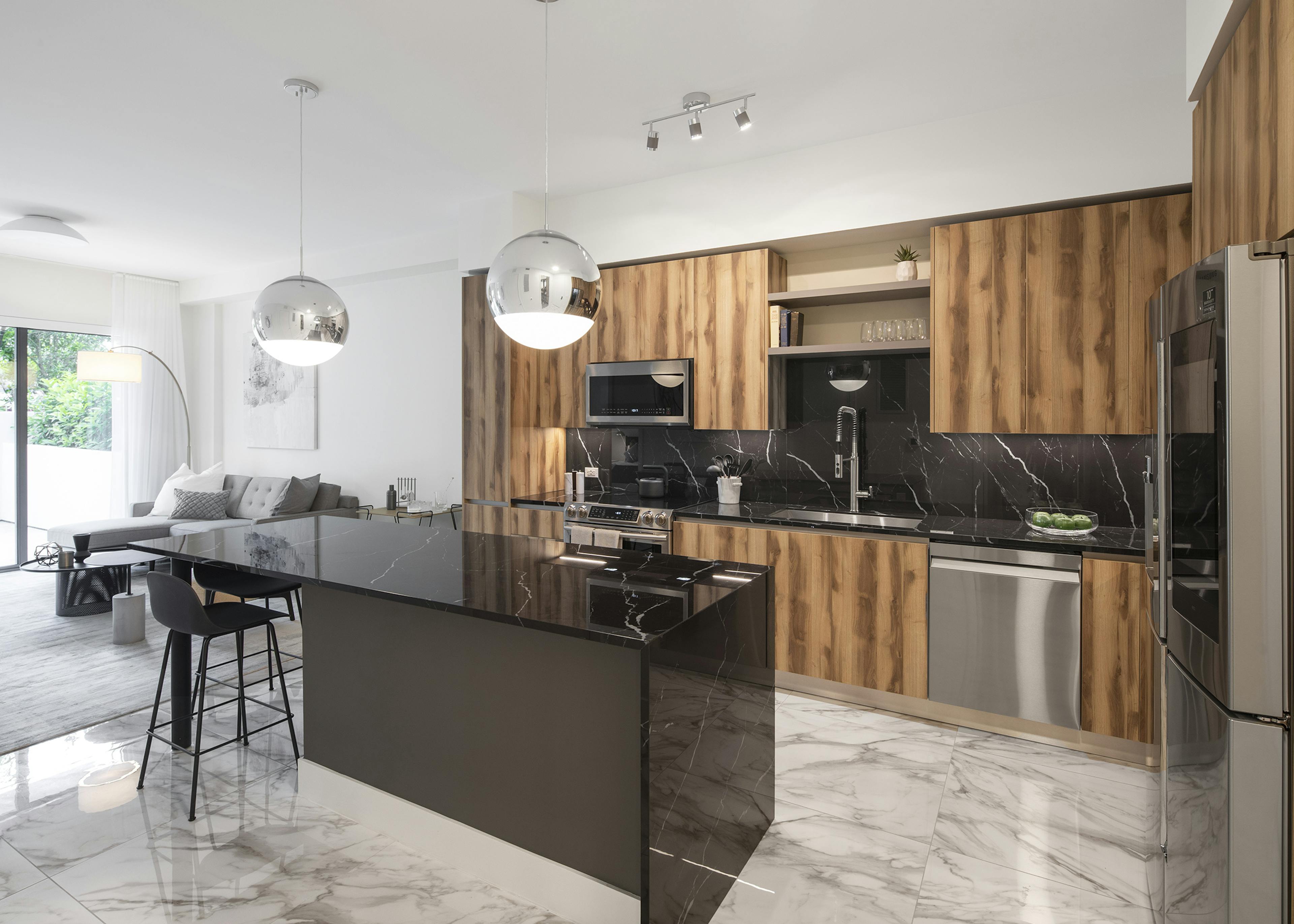 Interior view of AMLI Midtown Miami apartment kitchen with dark marble island and zebra wood cabinets and living room at left