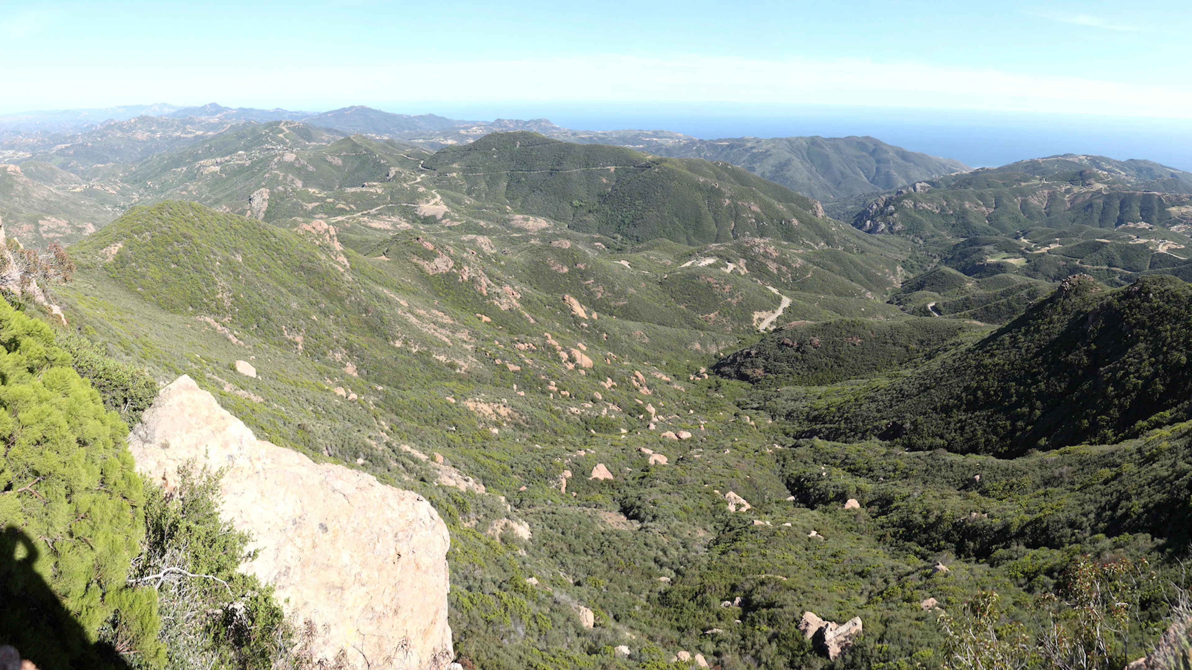 View from a small mountain down a lush green valley dotted with rocky outcroppings and the ocean in the far distance