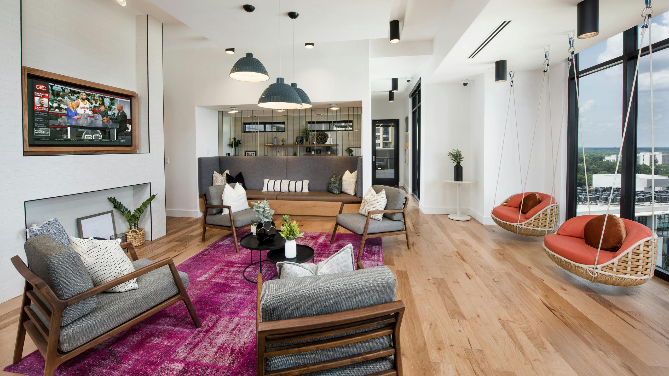 AMLI Lenox sky lounge with bright pink rug and multiple seating areas and a TV and two swings near large windows