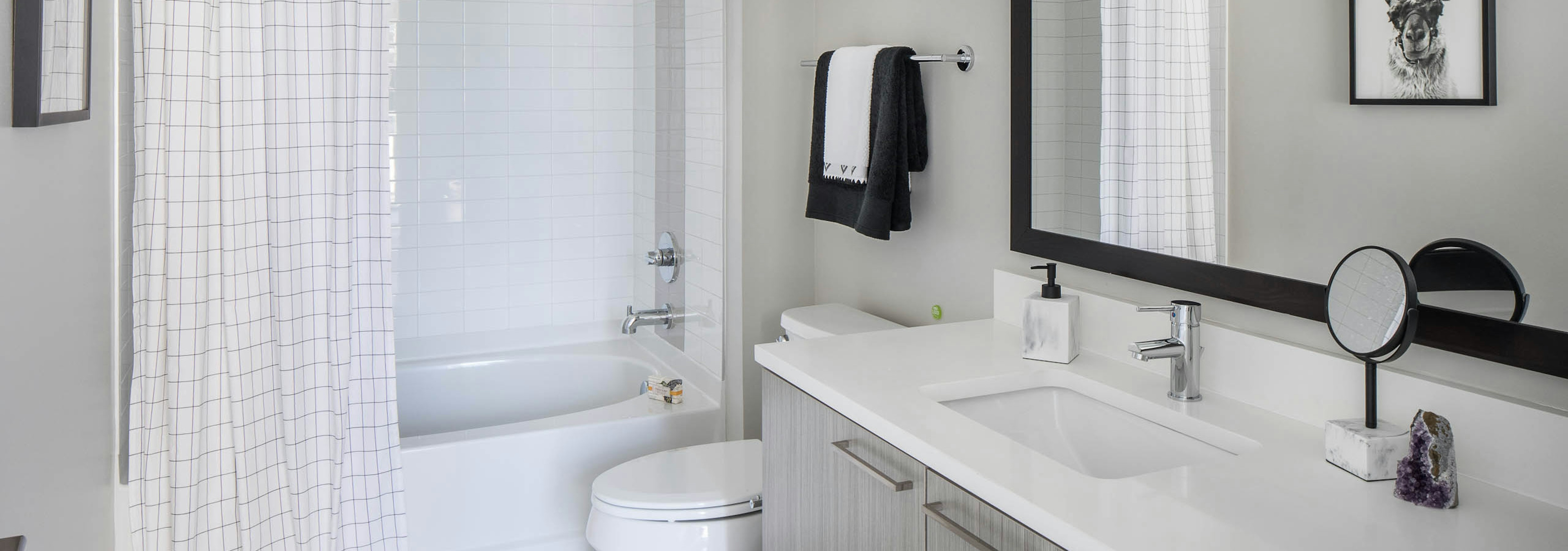 AMLI Arts Center bathroom with grey wood vanity sink and white bathtub with a plaid curtain and black towel above the toilet