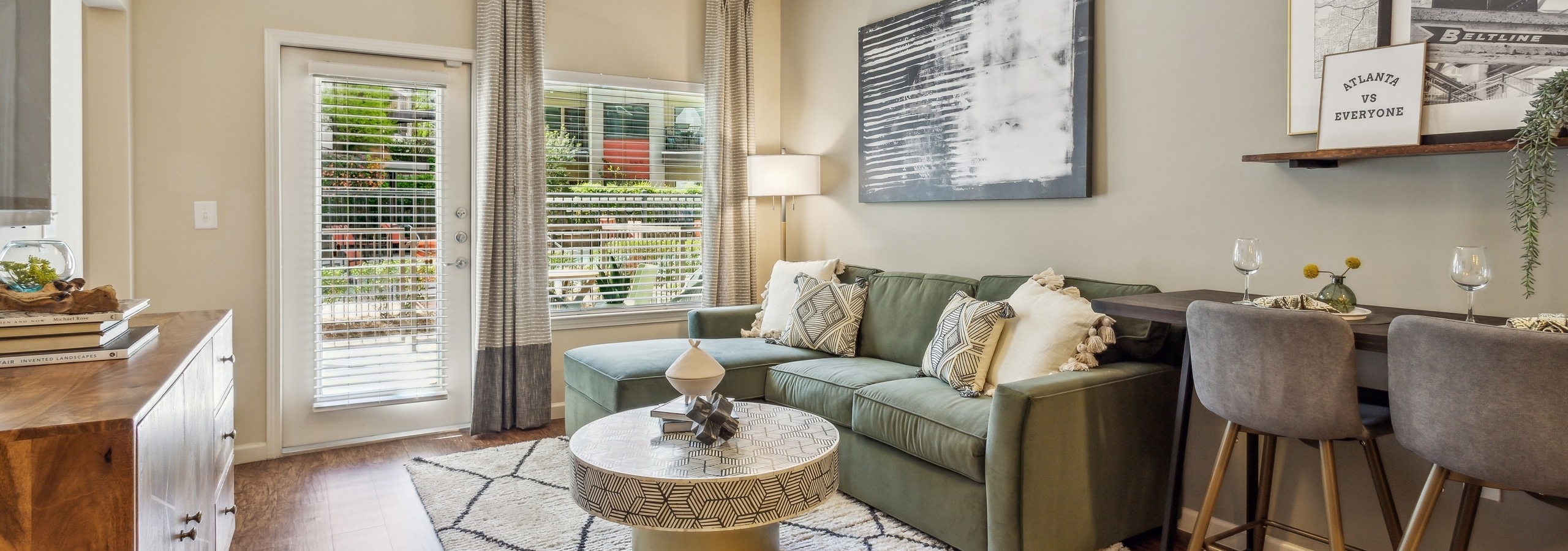 Living room at AMLI Ponce Park apartments with green couch on geometric area rug with windows with blinds and curtains