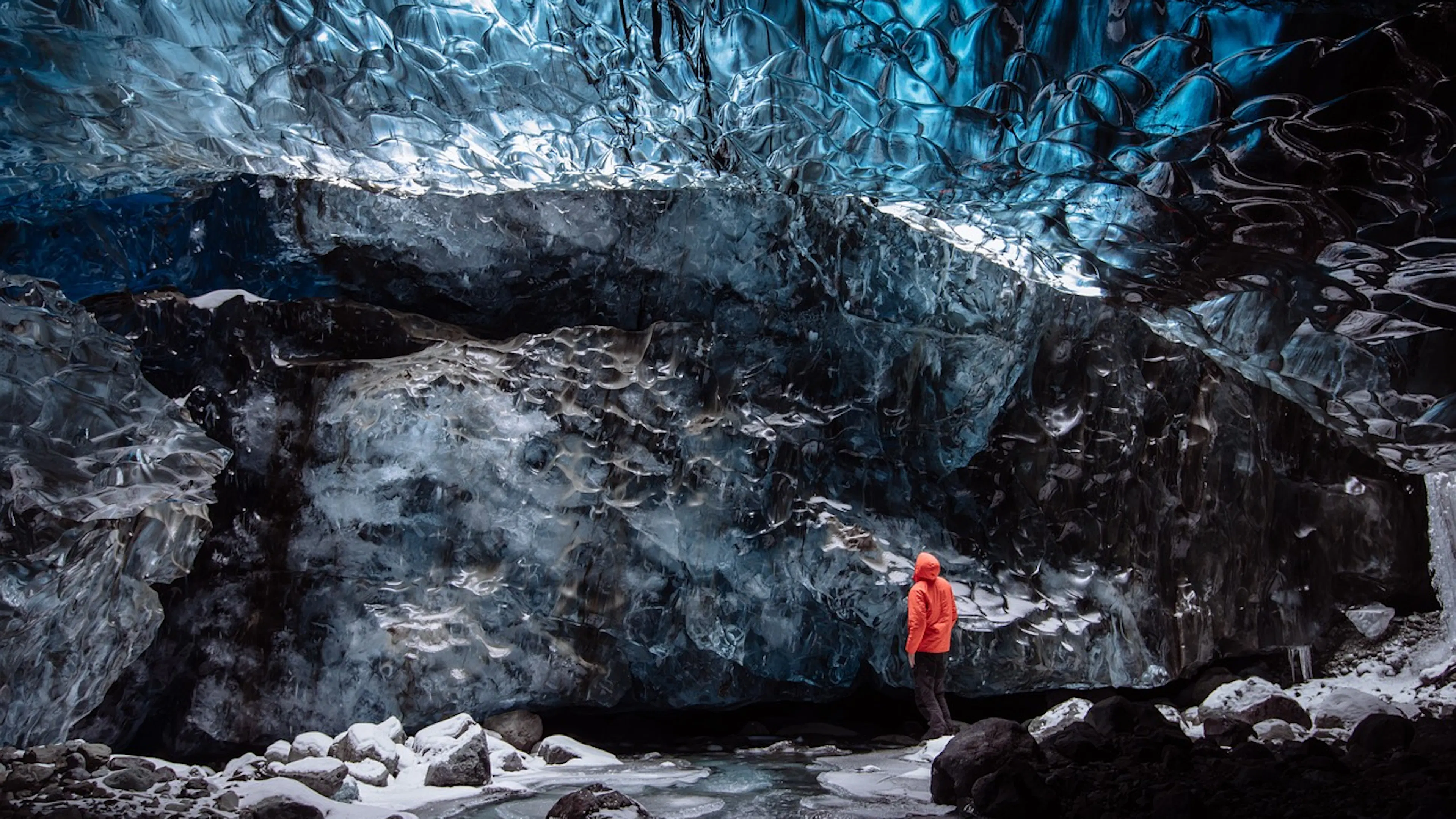 A hiker in an orange puffy jacket standing in the center of an ice cave