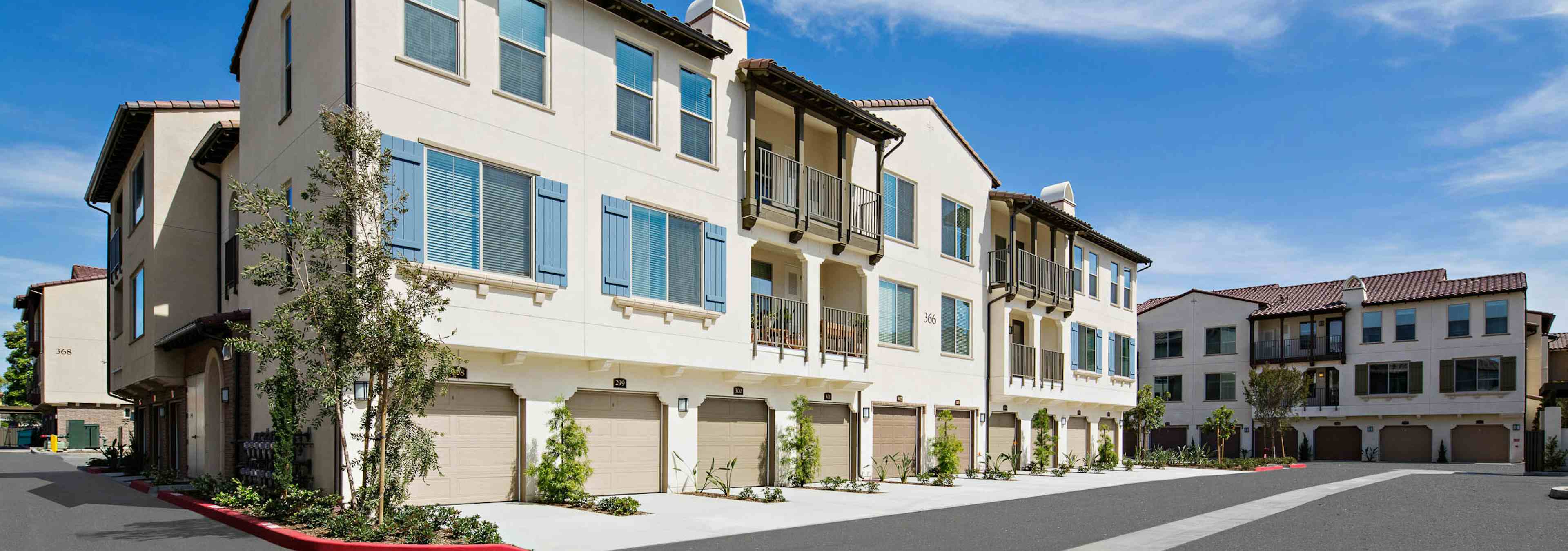 Exterior daytime rendering of driveway at AMLI Spanish HIlls apartments with blue window shutters, trees and garage doors