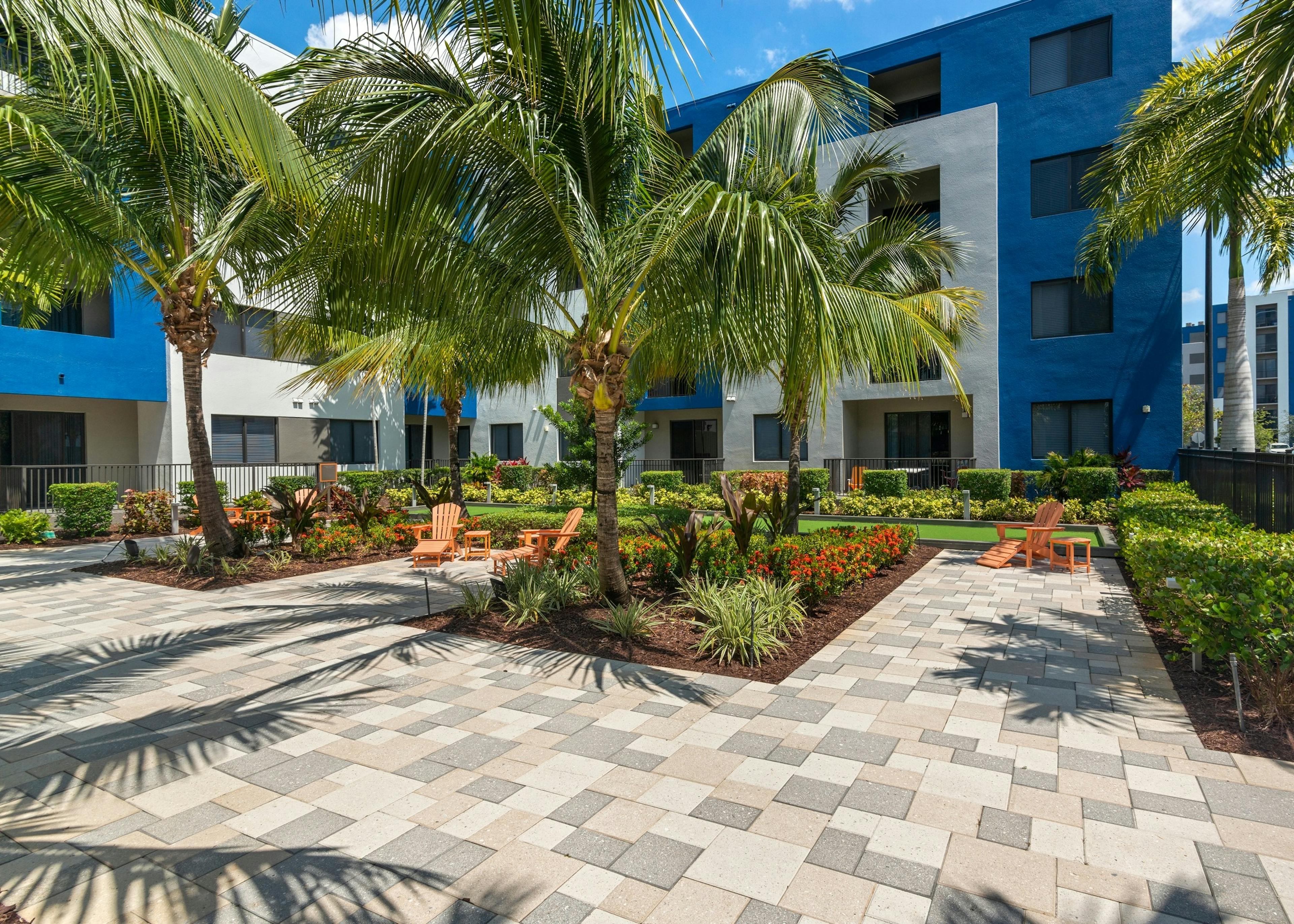 AMLI 8800 apartment building courtyard with lush tropical landscape and faux grass bocce ball court and orange armchairs 