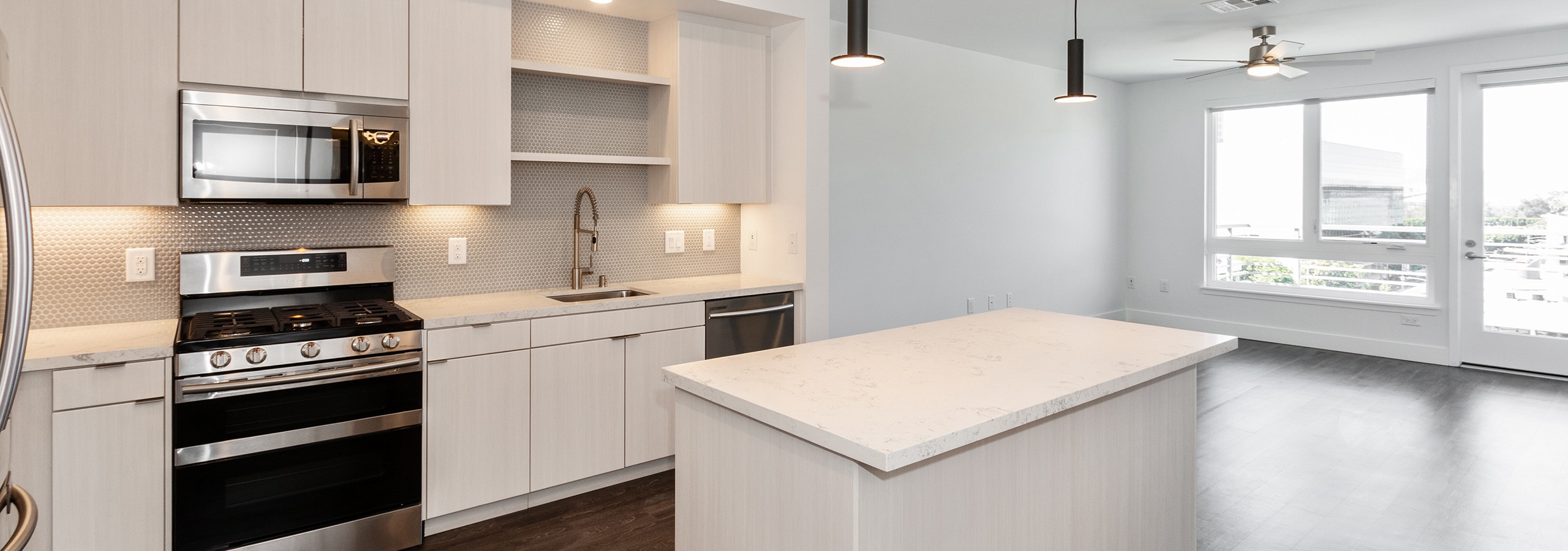 Interior of AMLI Park Broadway apartment kitchen with quartz countertops, white cabinetry facing living room and large window