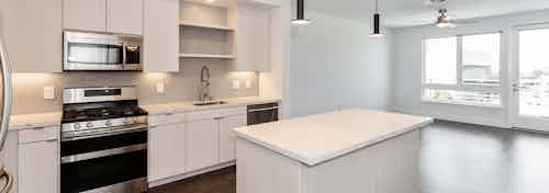 Interior of AMLI Park Broadway apartment kitchen with quartz countertops, white cabinetry facing living room and large window
