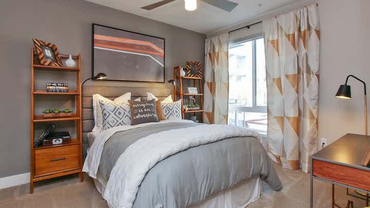 Interior view of AMLI Uptown Orange apartment bedroom with full bed, night stands and large window overlooking pool courtyard