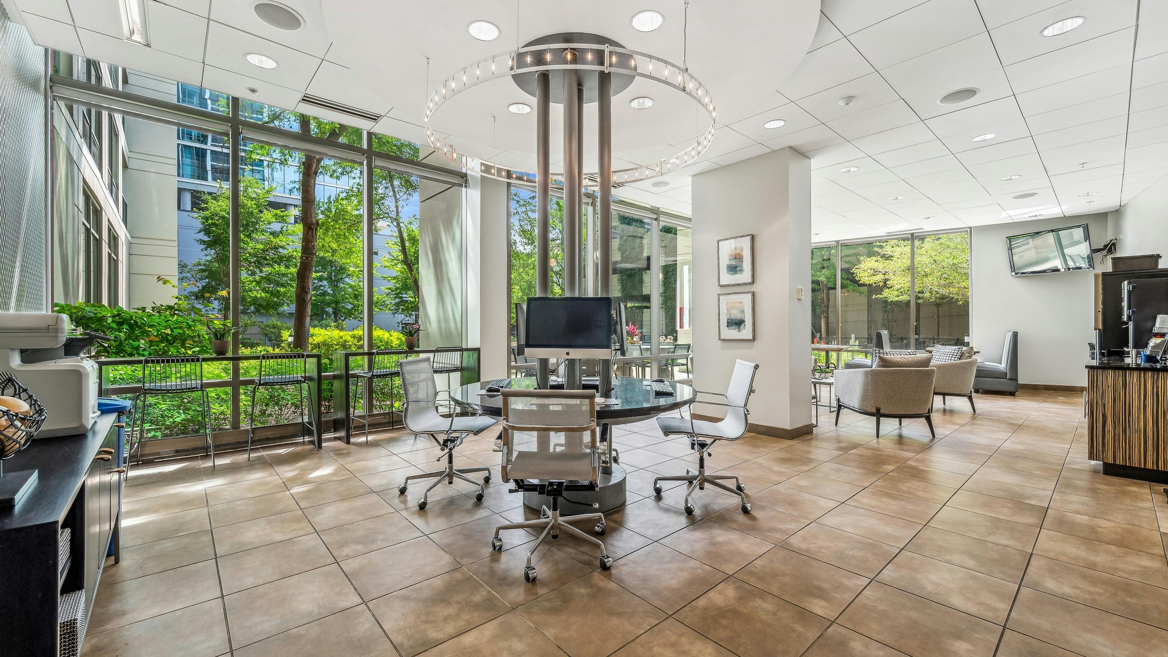 Business center at AMLI 900 with circular glass- top work station and white ceilings and brown tile floor with view to exterior
