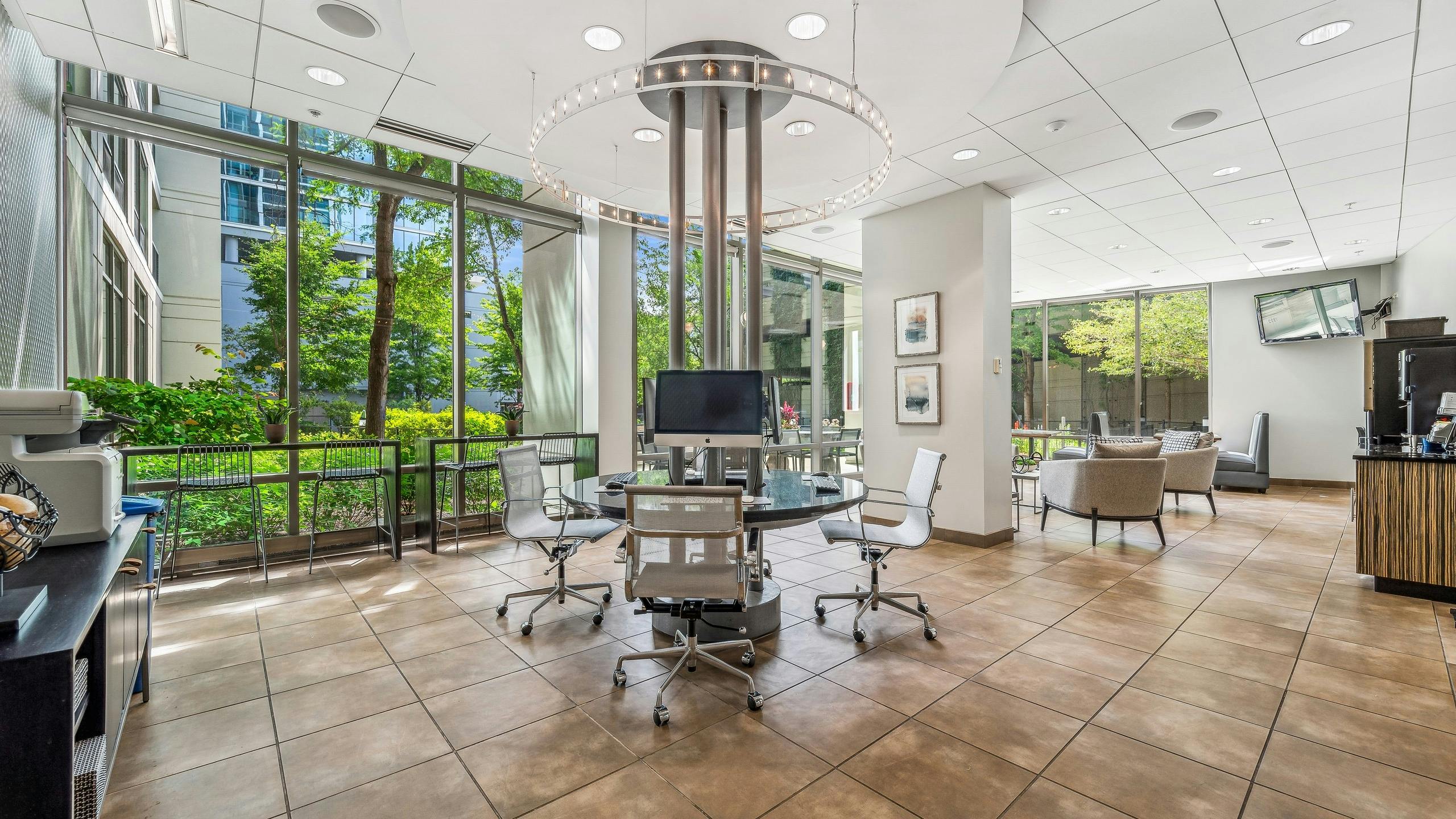 Business center at AMLI 900 with circular glass- top work station and white ceilings and brown tile floor with view to exterior