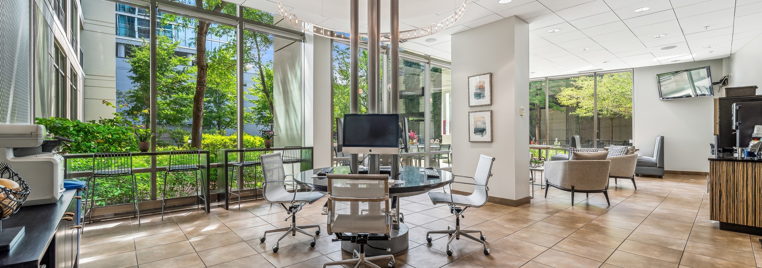 Business center at AMLI 900 with circular glass- top work station and white ceilings and brown tile floor with view to exterior