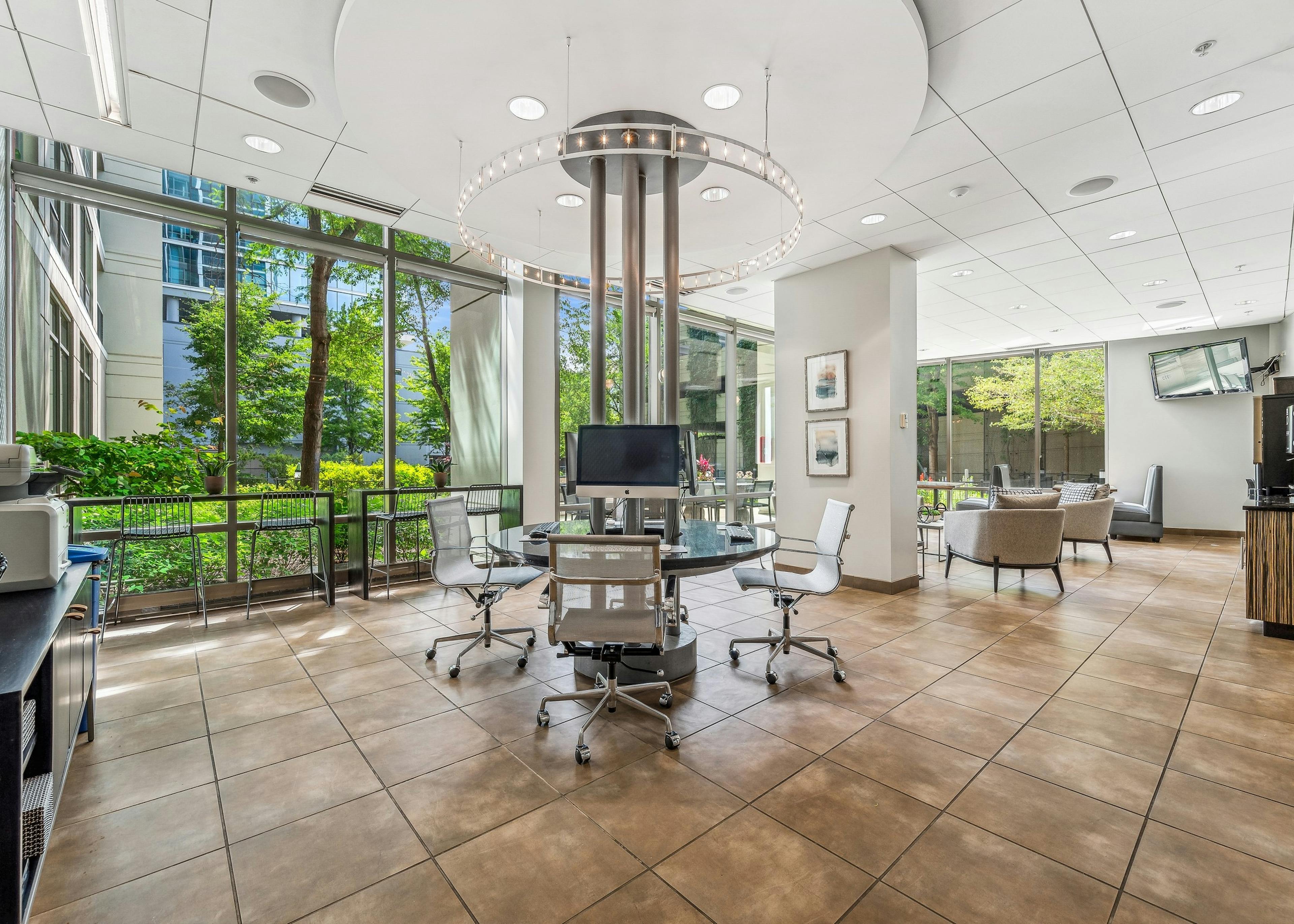 Business center at AMLI 900 with circular glass- top work station and white ceilings and brown tile floor with view to exterior