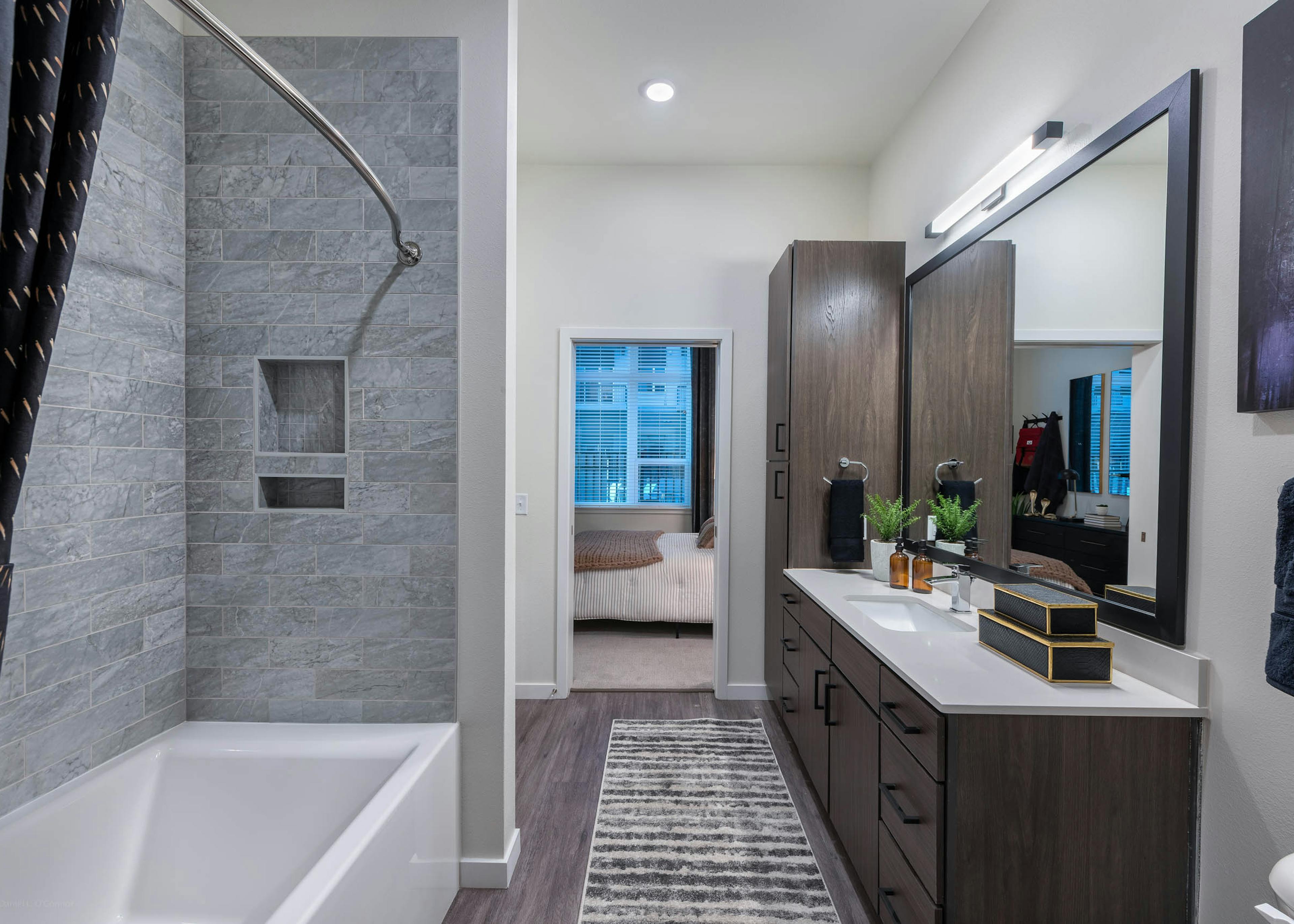 Interior of a bathroom at AMLI Art District with shower with gray marble tile and a sink with mirror and look into bedroom