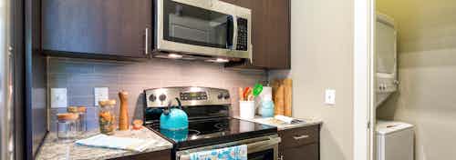 Close up of AMLI at Mueller dark kitchen cabinetry with beige backsplash and granite countertops with peek into laundry area