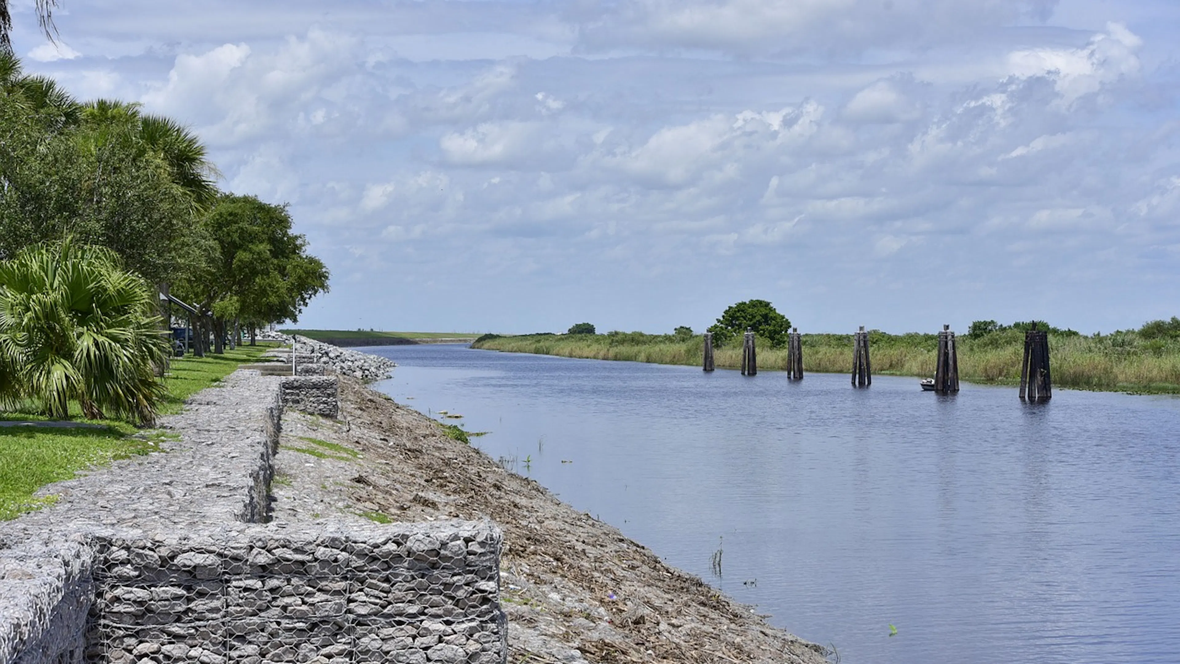 A stone wall running alongside a canal that leads into a large freshwater lake and marsh