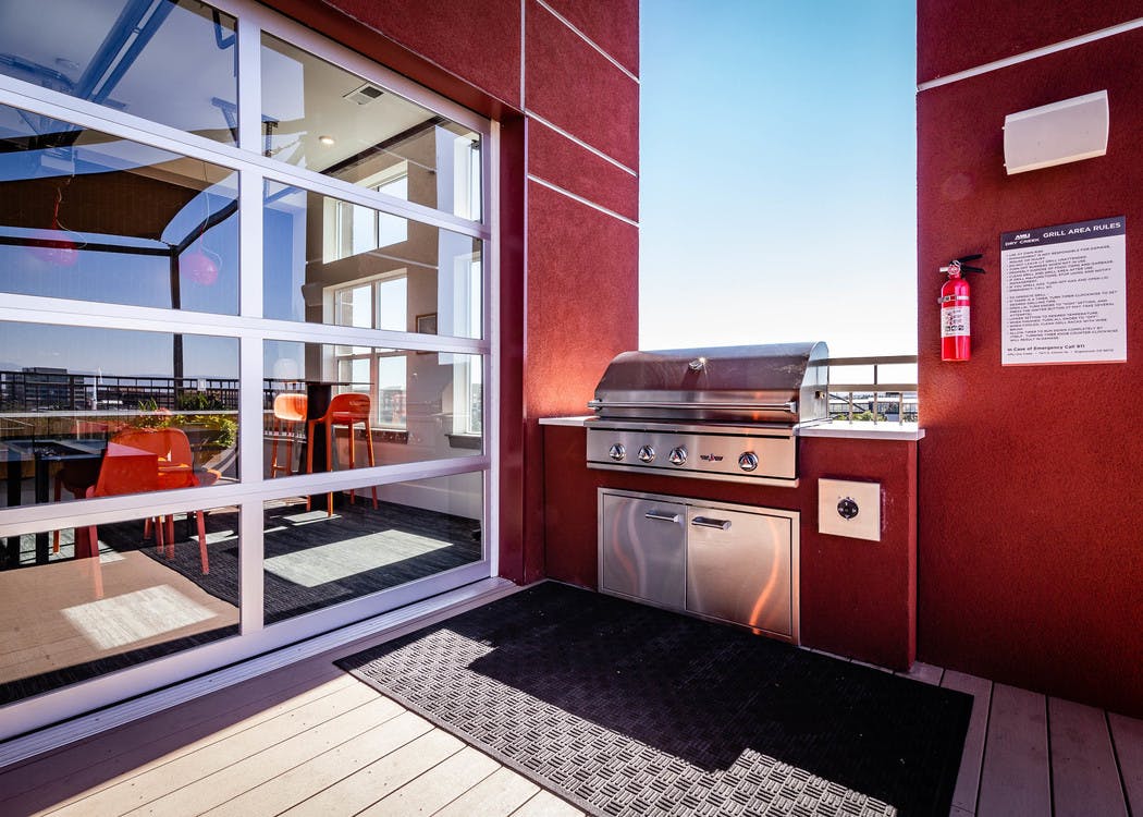 The roof top barbeque area at AMLI Dry Creek apartments with grill and glass garage door with view of lounge with television