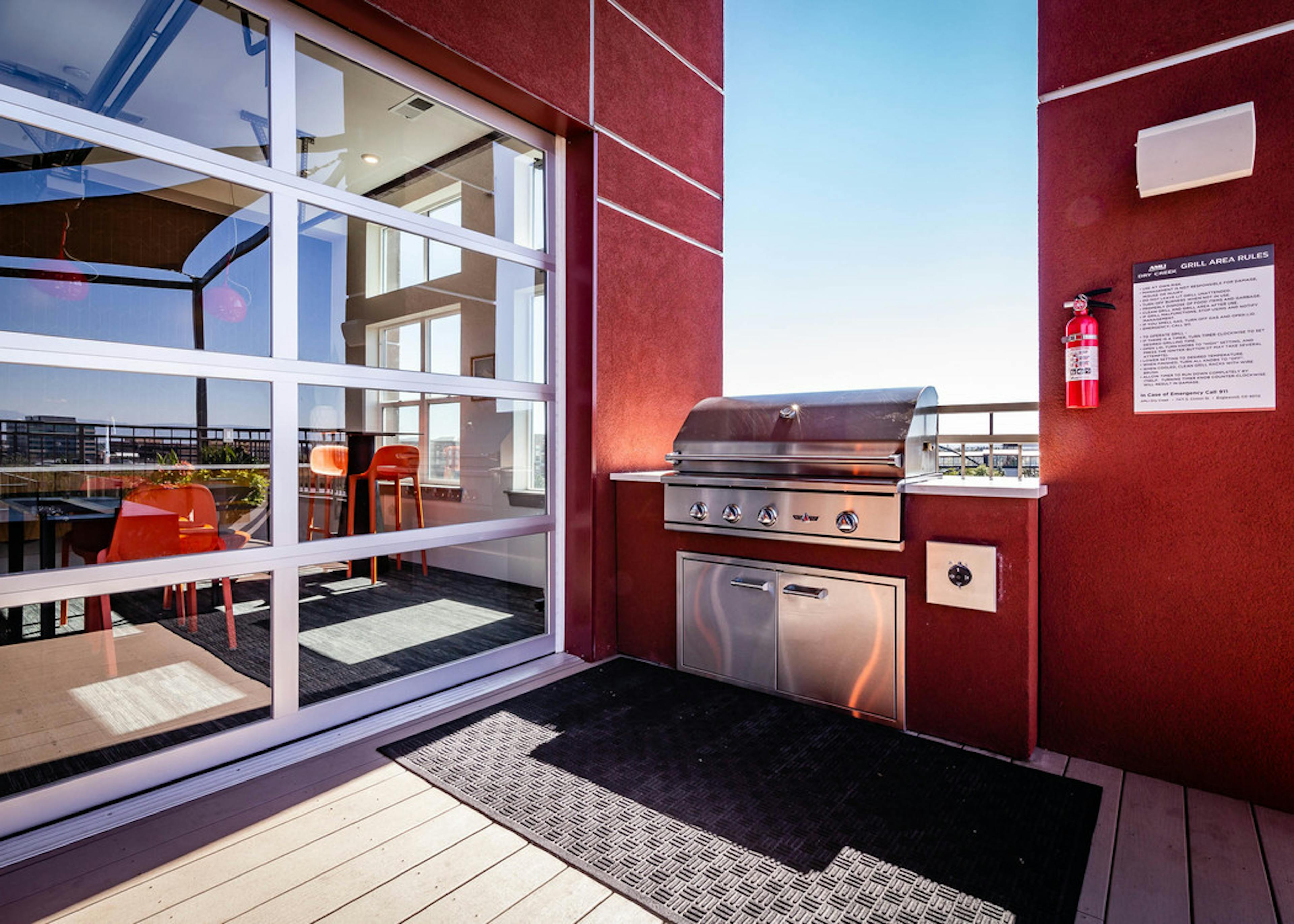 The roof top barbeque area at AMLI Dry Creek apartments with grill and glass garage door with view of lounge with television