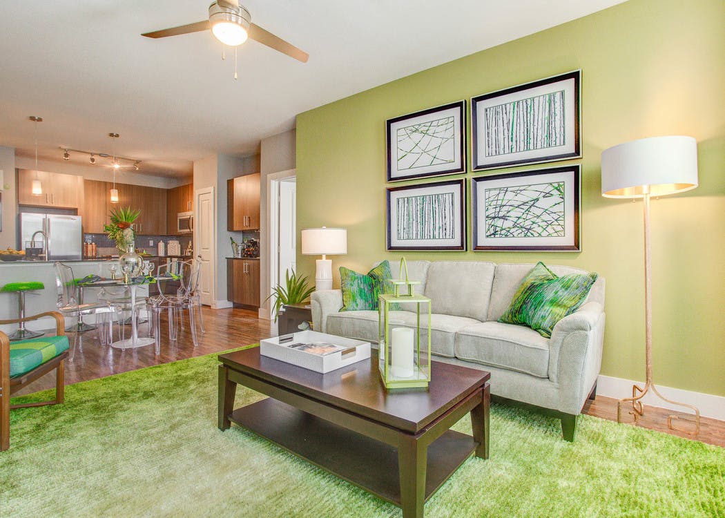 A living room at AMLI Riverfront Park apartments with couches and lamps and a green color scheme with a view into the kitchen