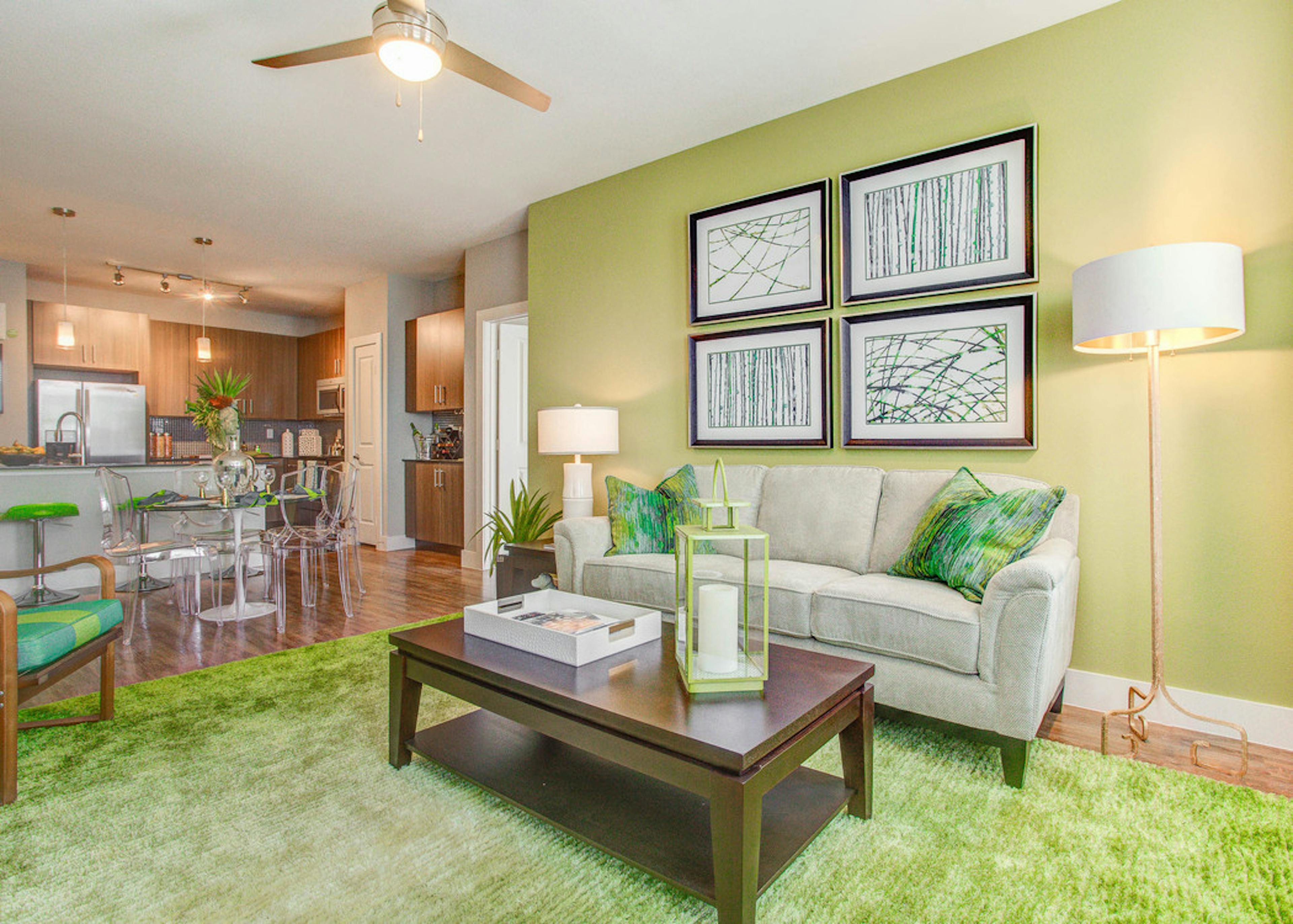 A living room at AMLI Riverfront Park apartments with couches and lamps and a green color scheme with a view into the kitchen