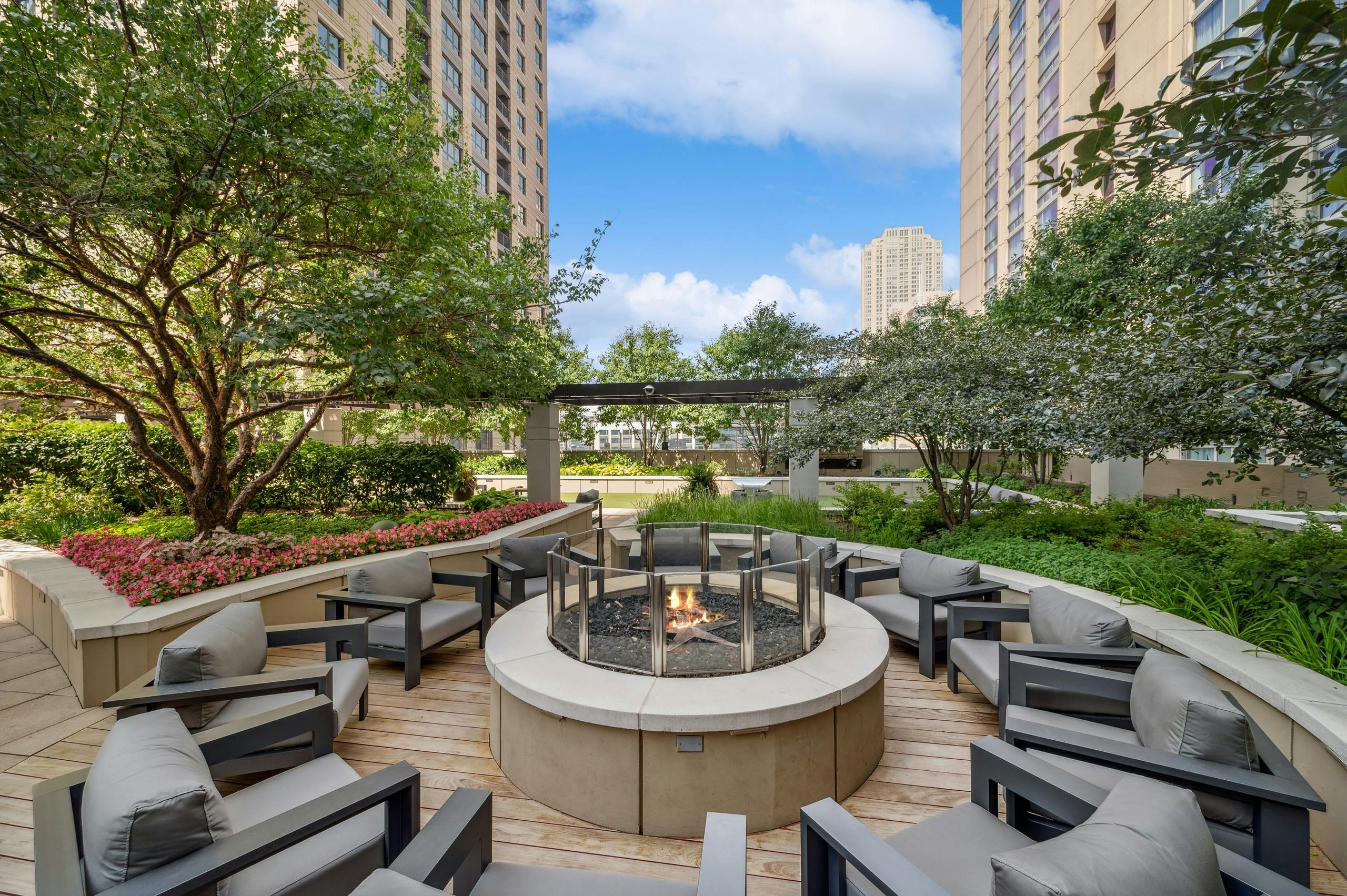 Rooftop firepit at AMLI River North with surrounding green foliage and gray chairs centered around a firepit with a flame