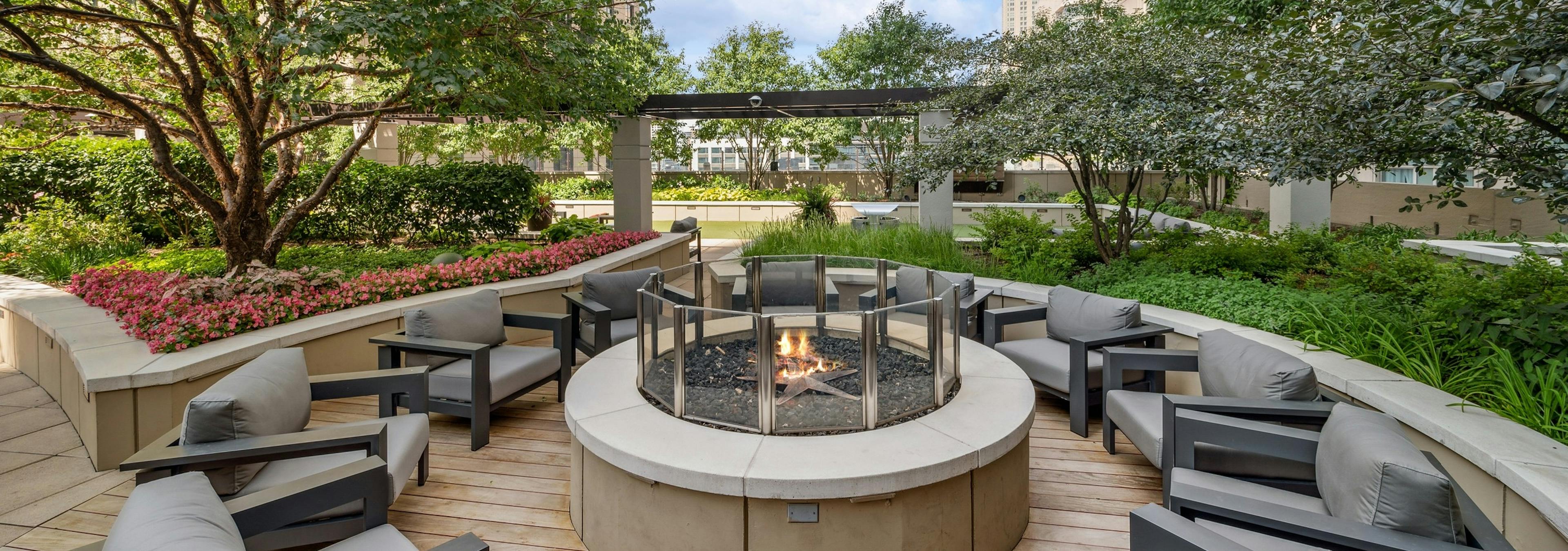 Rooftop firepit at AMLI River North with surrounding green foliage and gray chairs centered around a firepit with a flame