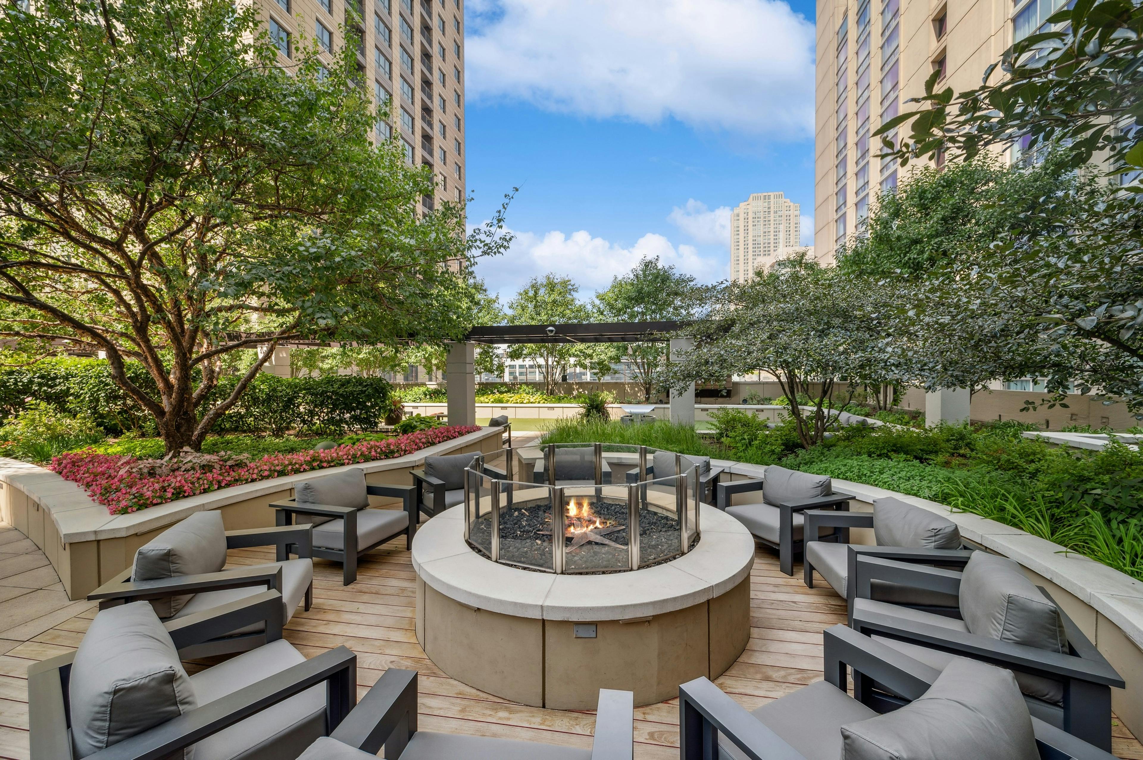 Rooftop firepit at AMLI River North with surrounding green foliage and gray chairs centered around a firepit with a flame