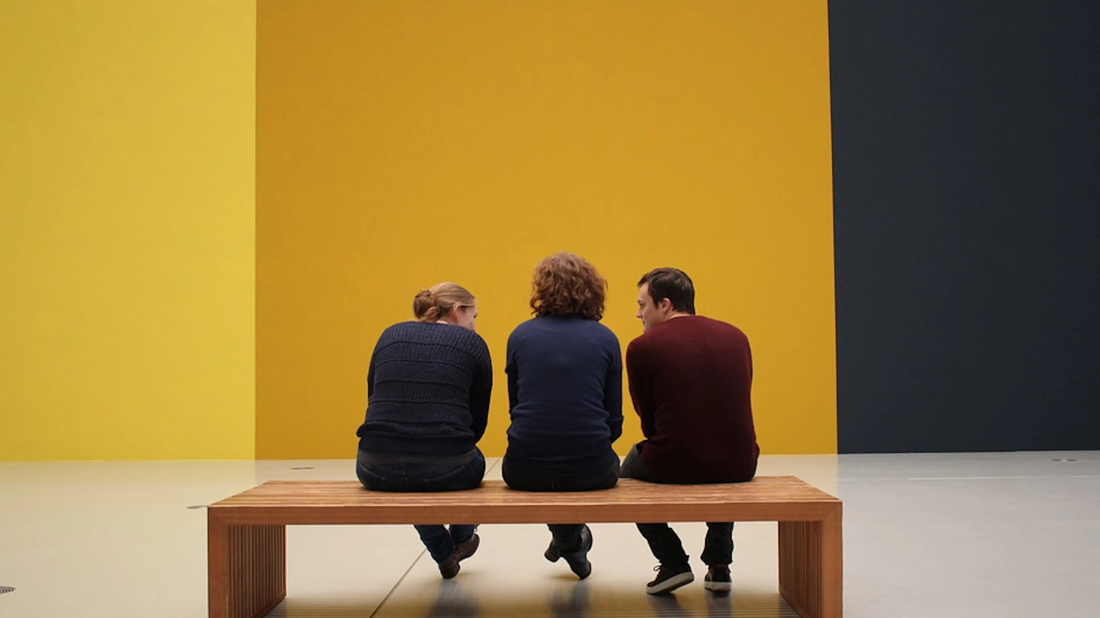 Three guests facing toward a large wall painted with three bold stripes of yellows and black