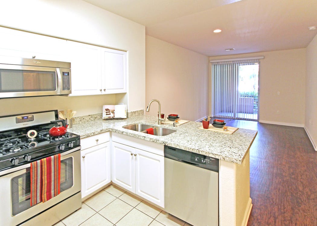 AMLI Warner Center apartment kitchen with white cabinets, stainless steel appliances and living room with hardwood floors