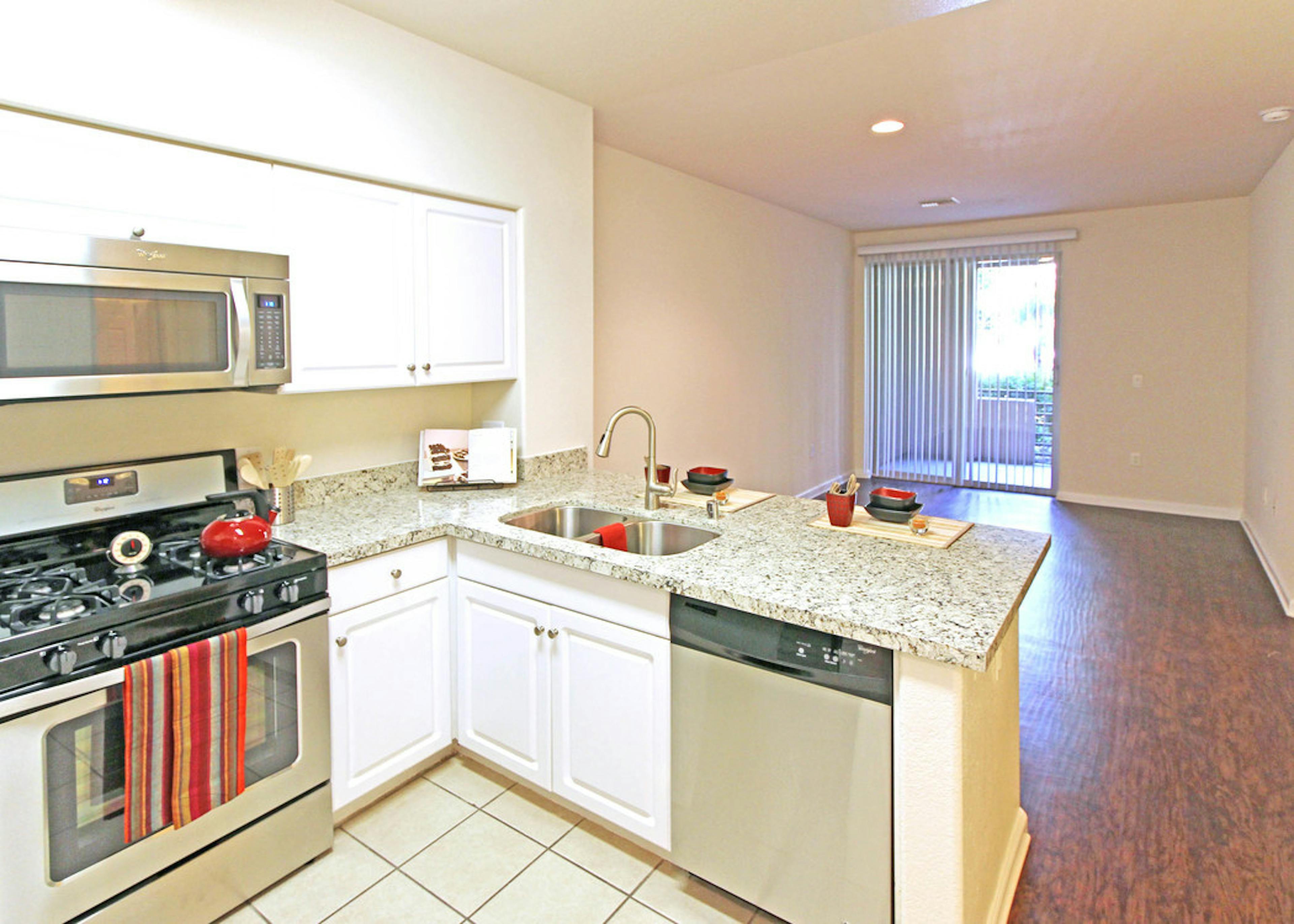 AMLI Warner Center apartment kitchen with white cabinets, stainless steel appliances and living room with hardwood floors