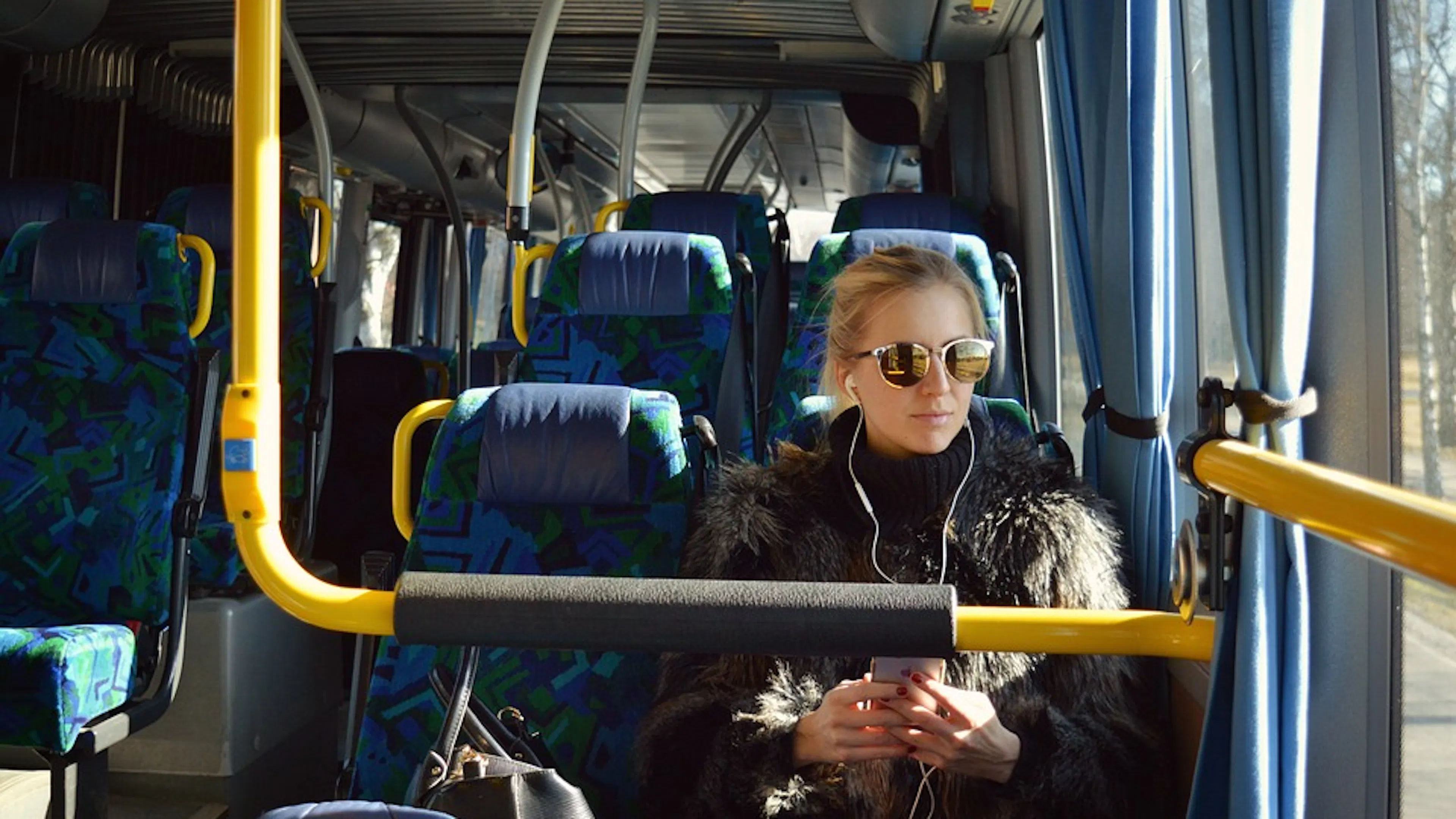 A woman with earphones plugged in sitting in a bus next to a large window