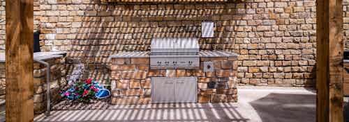 A barbeque area at AMLI Dry Creek apartments with cement counters and a wooden awning and a stone wall in the background