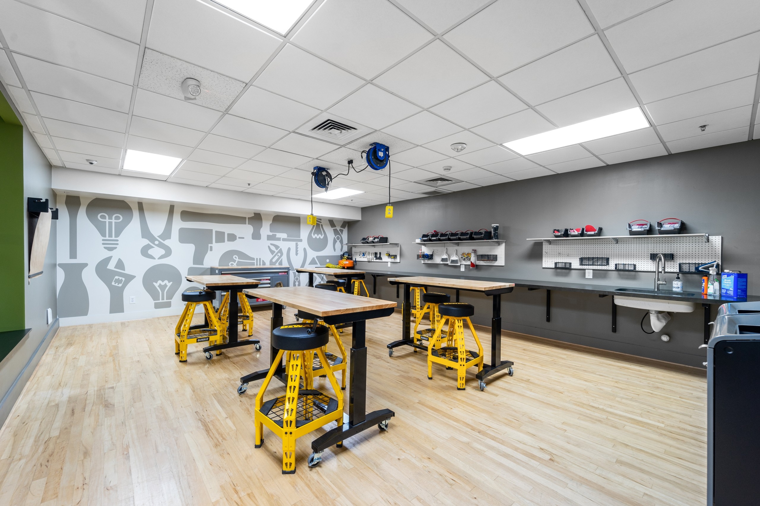 AMLI Bellevue Park maker lab with wood worktables with yellow and black stools and wall of tools and wall with tool graphics