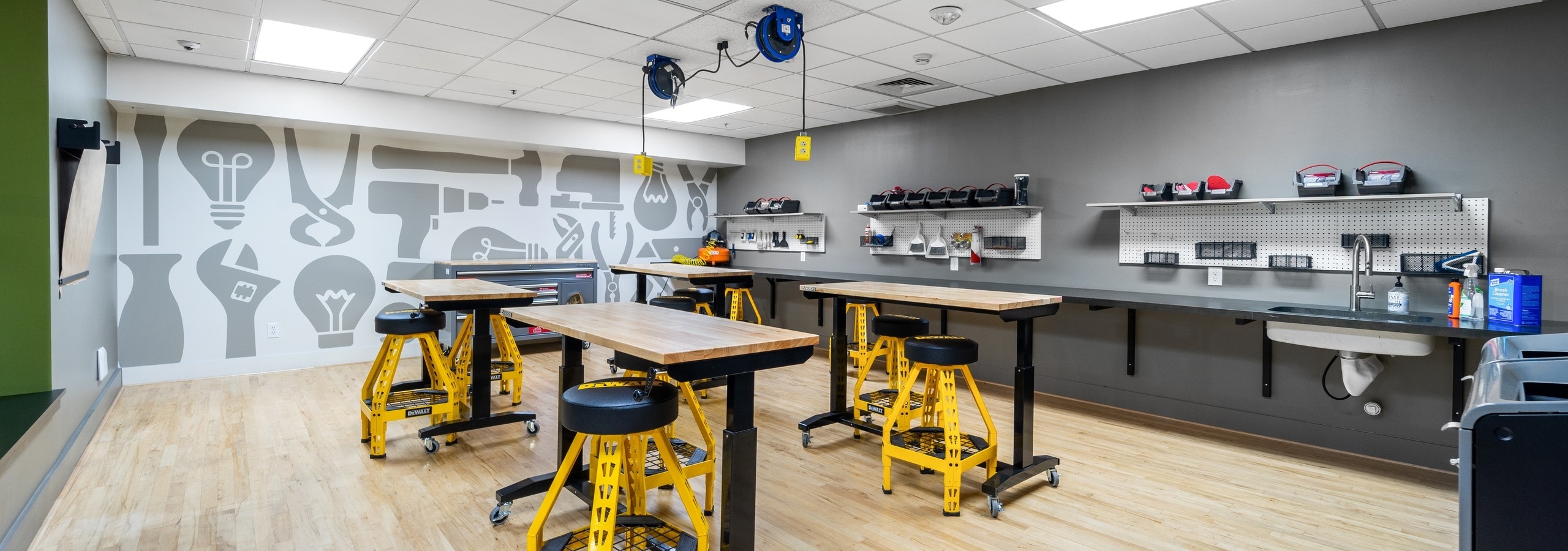 AMLI Bellevue Park maker lab with wood worktables with yellow and black stools and wall of tools and wall with tool graphics