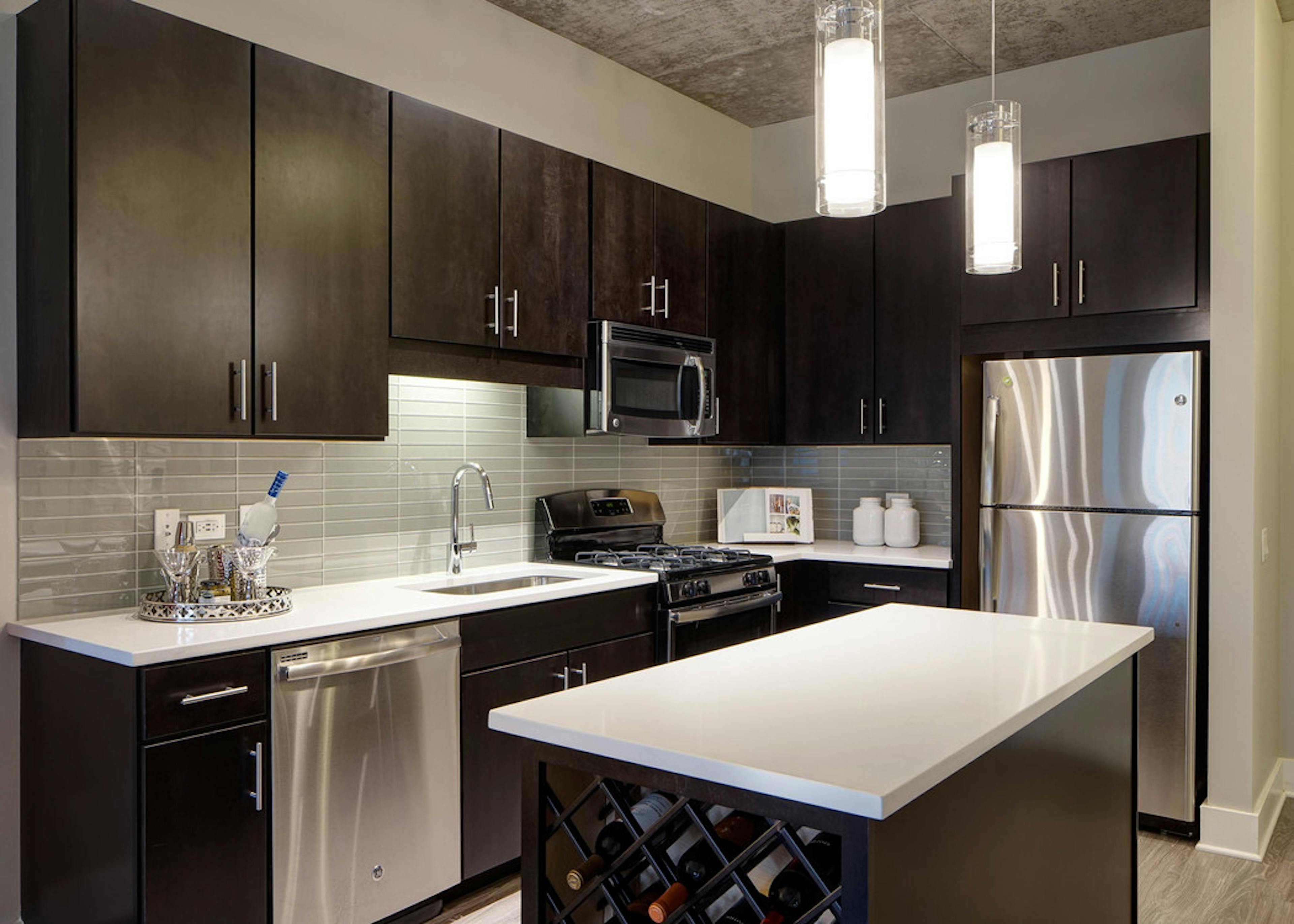 AMLI Lofts kitchen with a quartz island alongside dark wooden cabinets and a taupe backsplash with stainless steel appliances