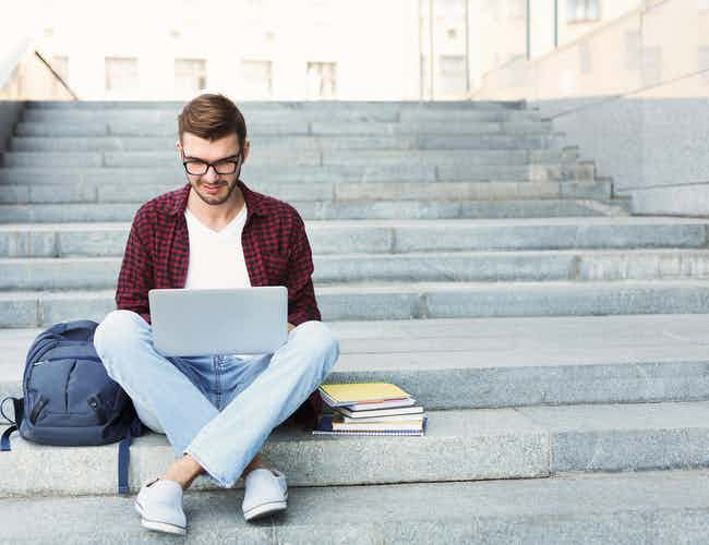 Guy studying with laptop and books on strps