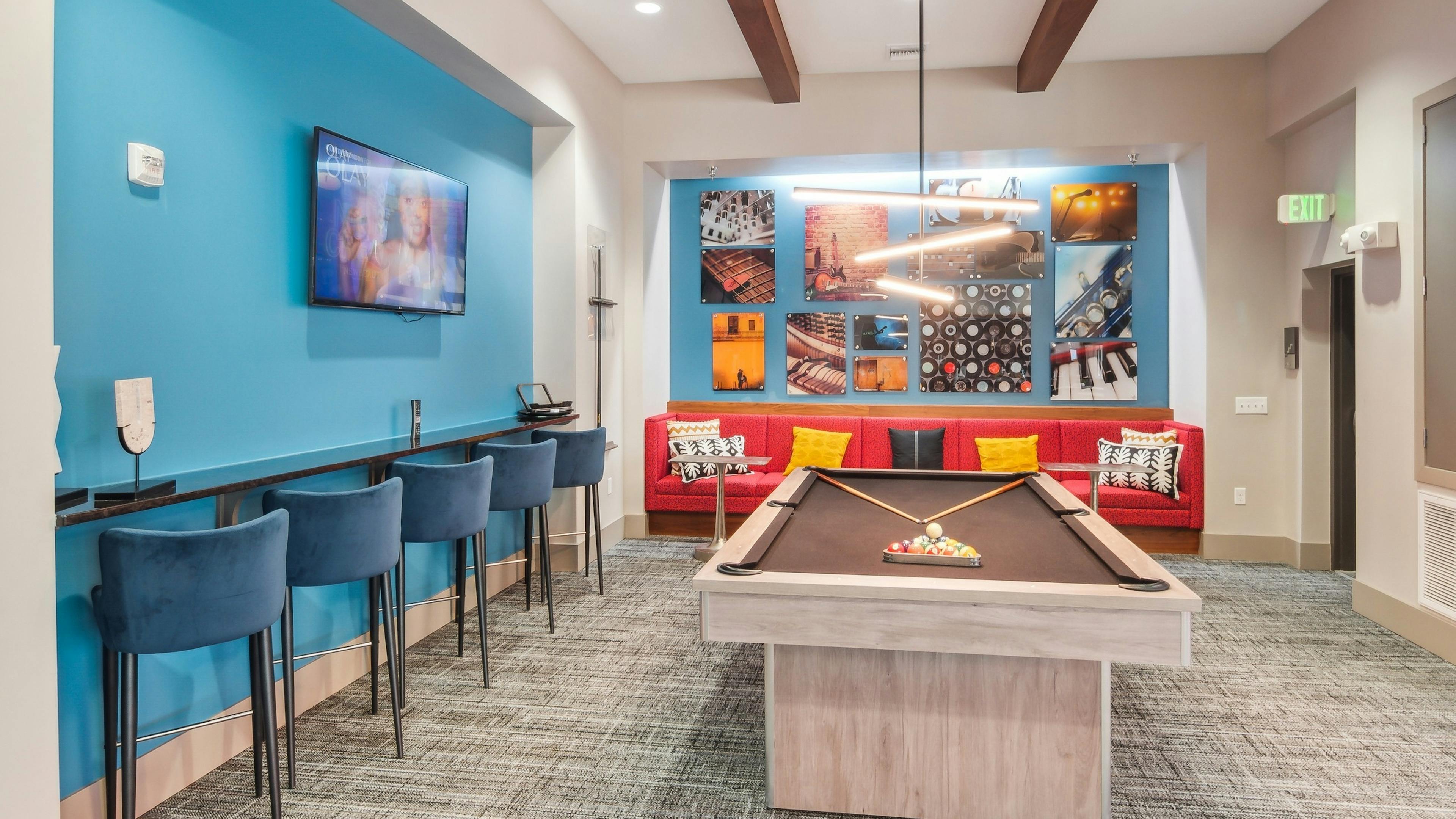 Interior view of the billiards table area at AMLI Denargo Market clubroom with red couch and blue walls with a TV and artwork