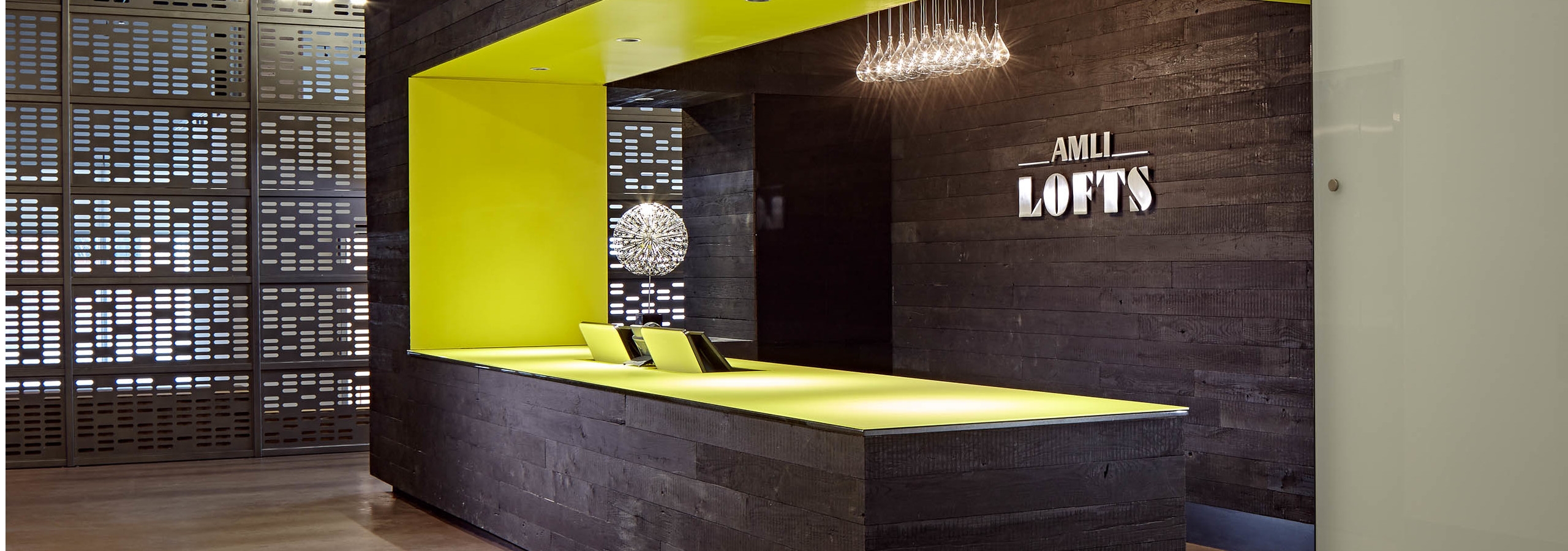 The Polk lobby at AMLI Lofts which has a deep brown textured accent wall and matching desk that has a vibrant yellow lining